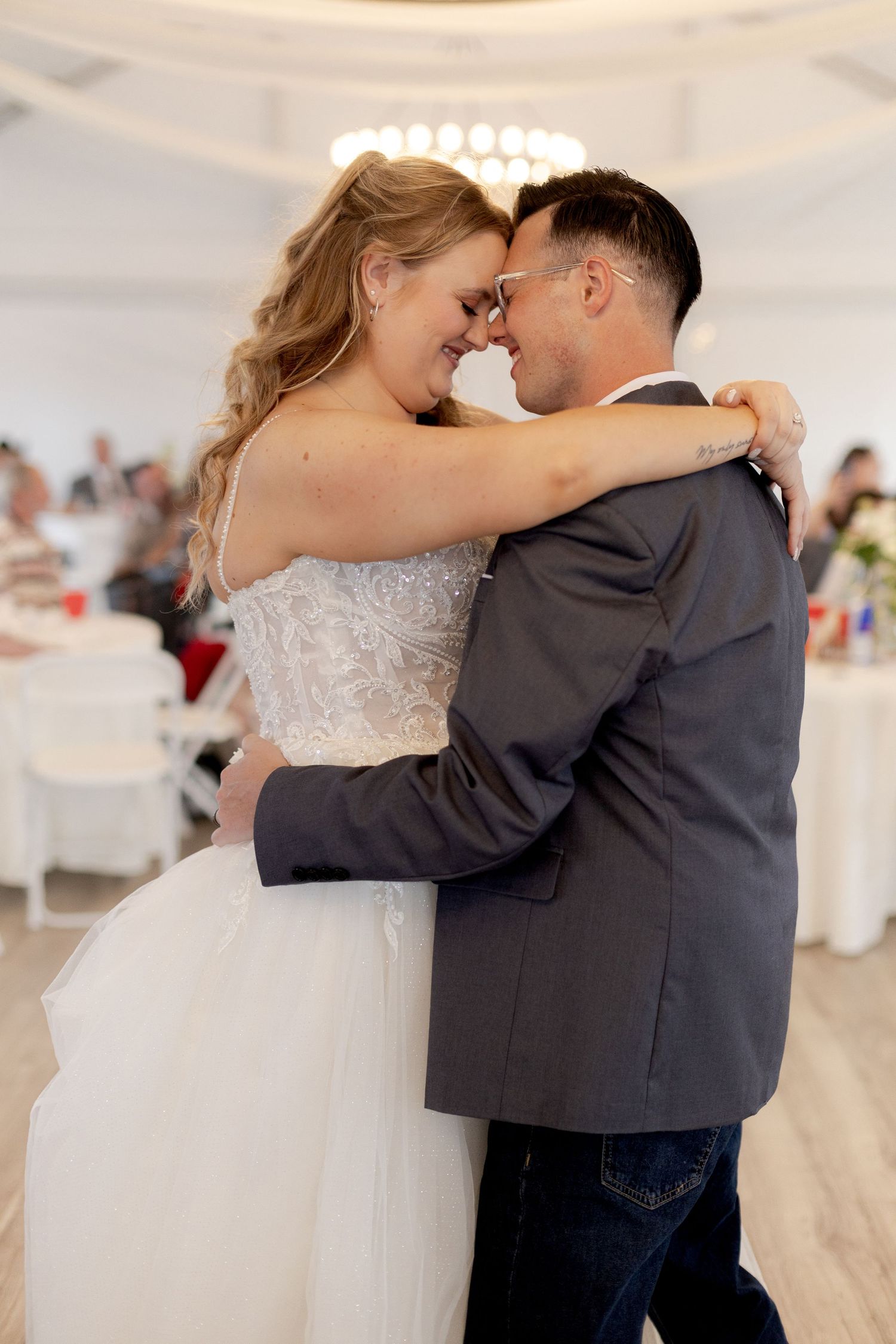 Bride and groom share their first dance, embracing closely with foreheads touching at their wedding reception.