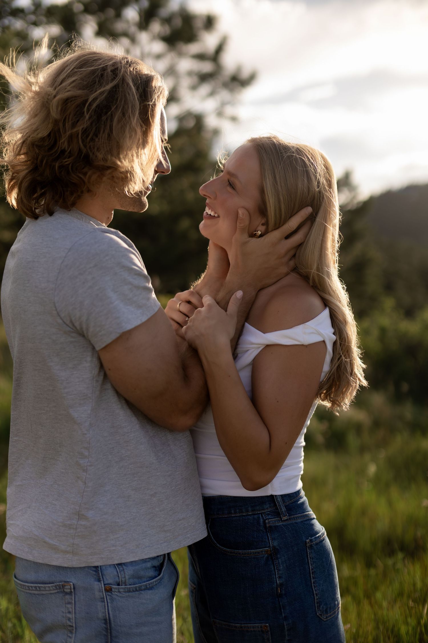 Man tenderly holding womans face as they smile at each other in a sunny outdoor field setting.