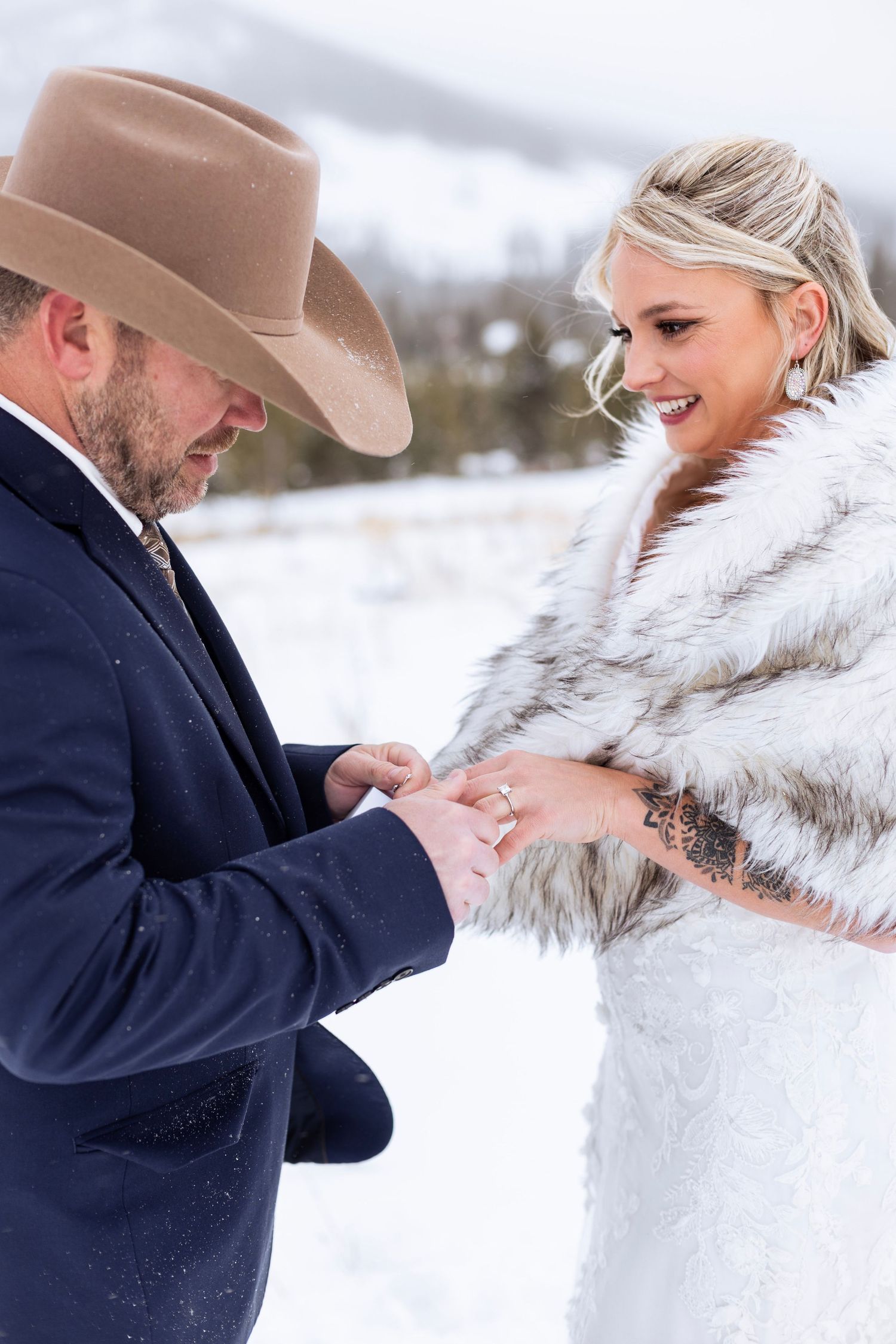 A winter wedding scene shows a couple exchanging rings in the snow, with the groom wearing a cowboy hat and navy suit.