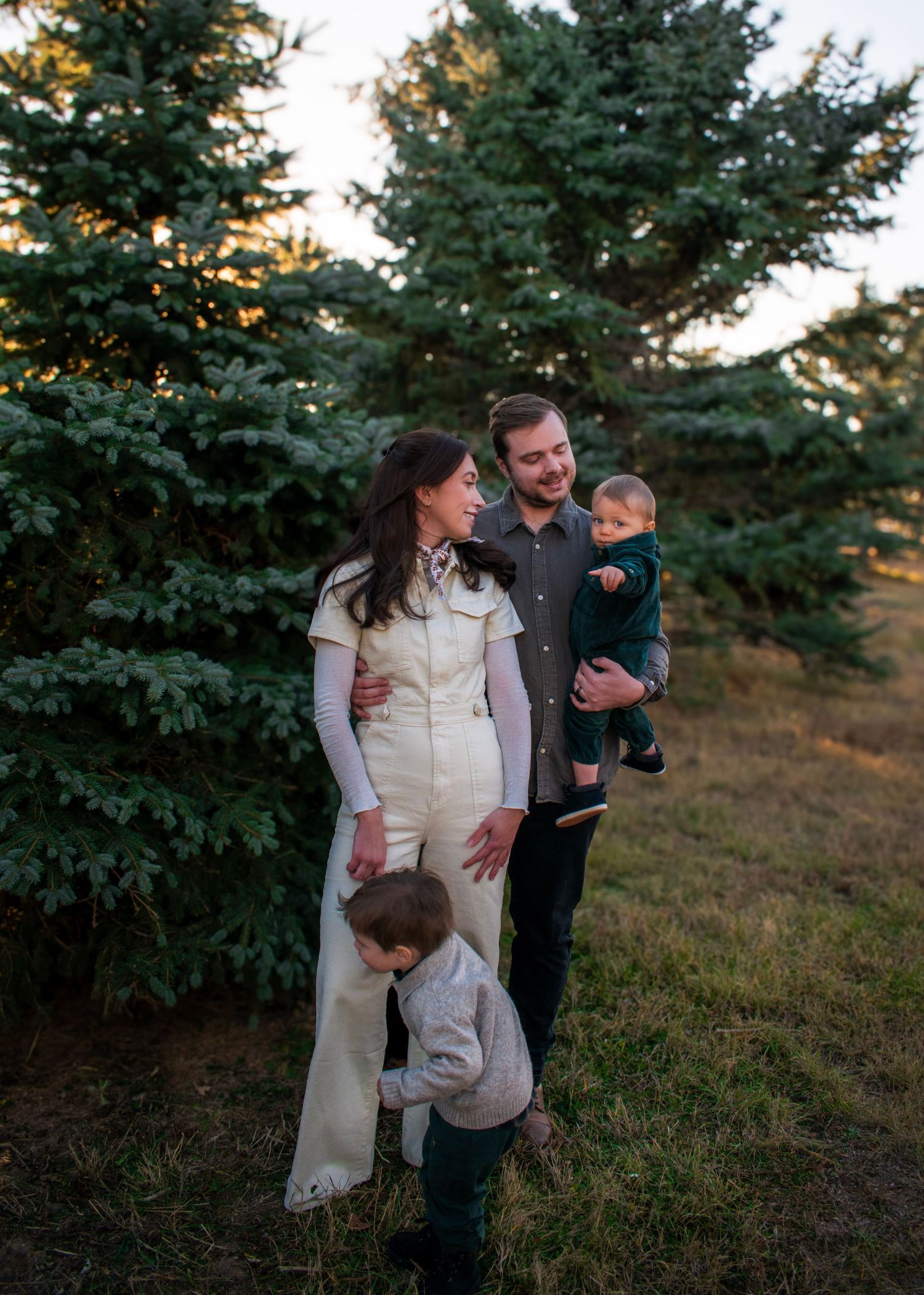 A family shares candid moments together near evergreen trees during golden hour.