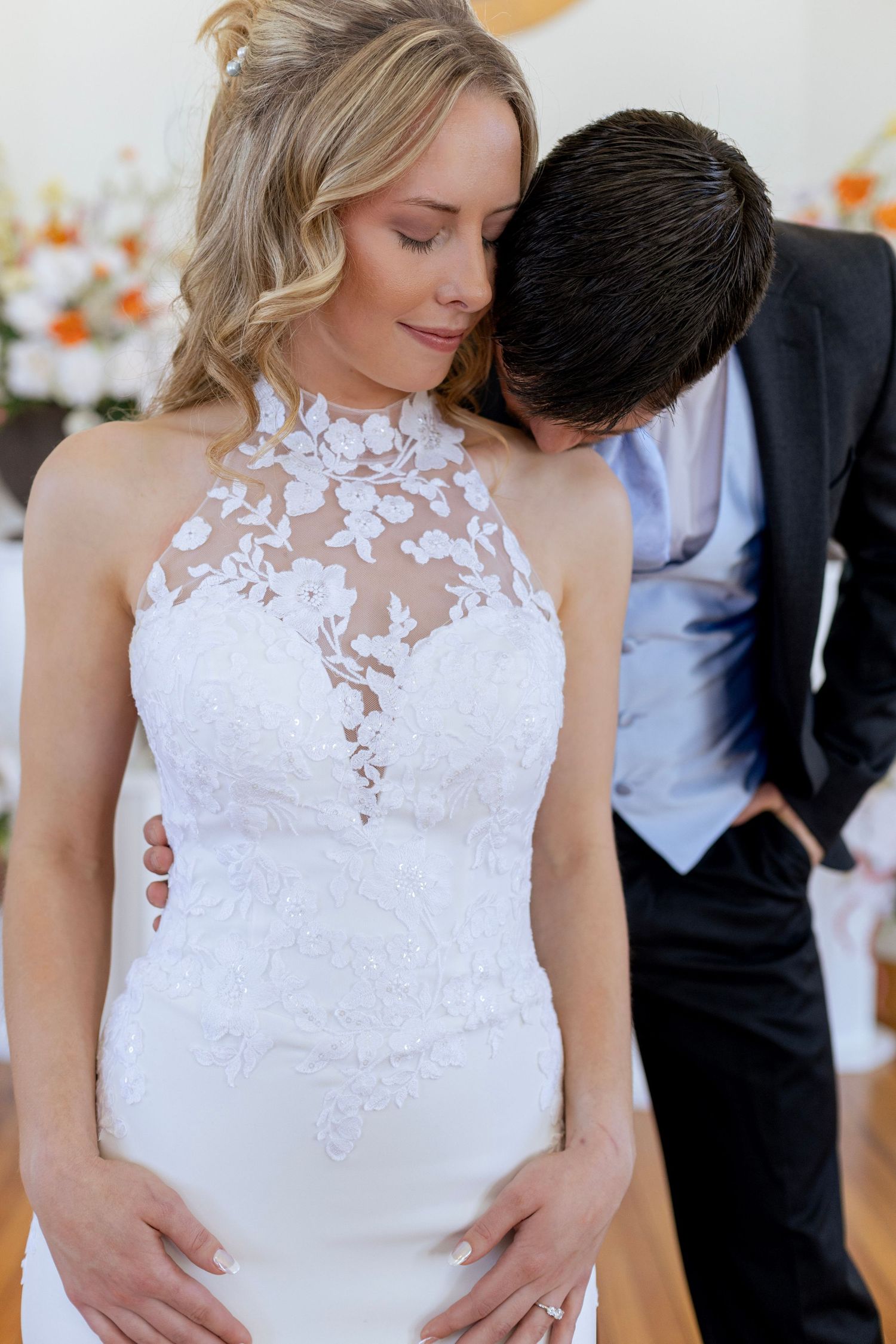 Groom tenderly kisses bride on the neck as she stands in a lace halter wedding gown at the altar.