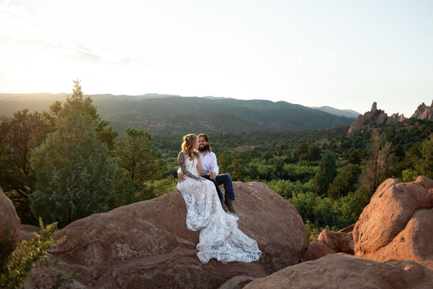 Bride and groom sitting on red rocks at sunset with mountain views at Garden of the Gods, Colorado.
