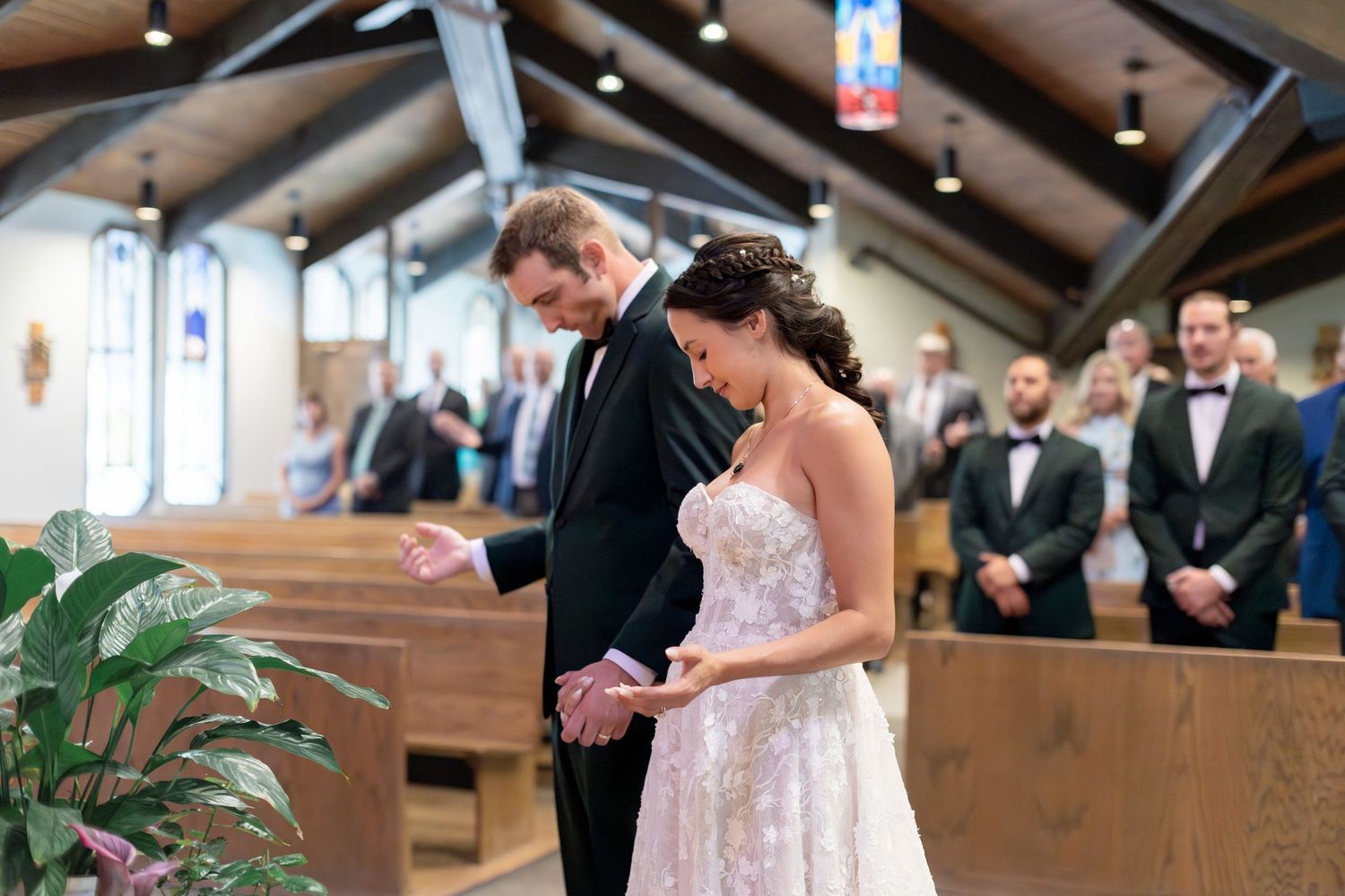 Bride and groom holding hands at church altar during wedding ceremony, guests seated in wooden pews behind them.