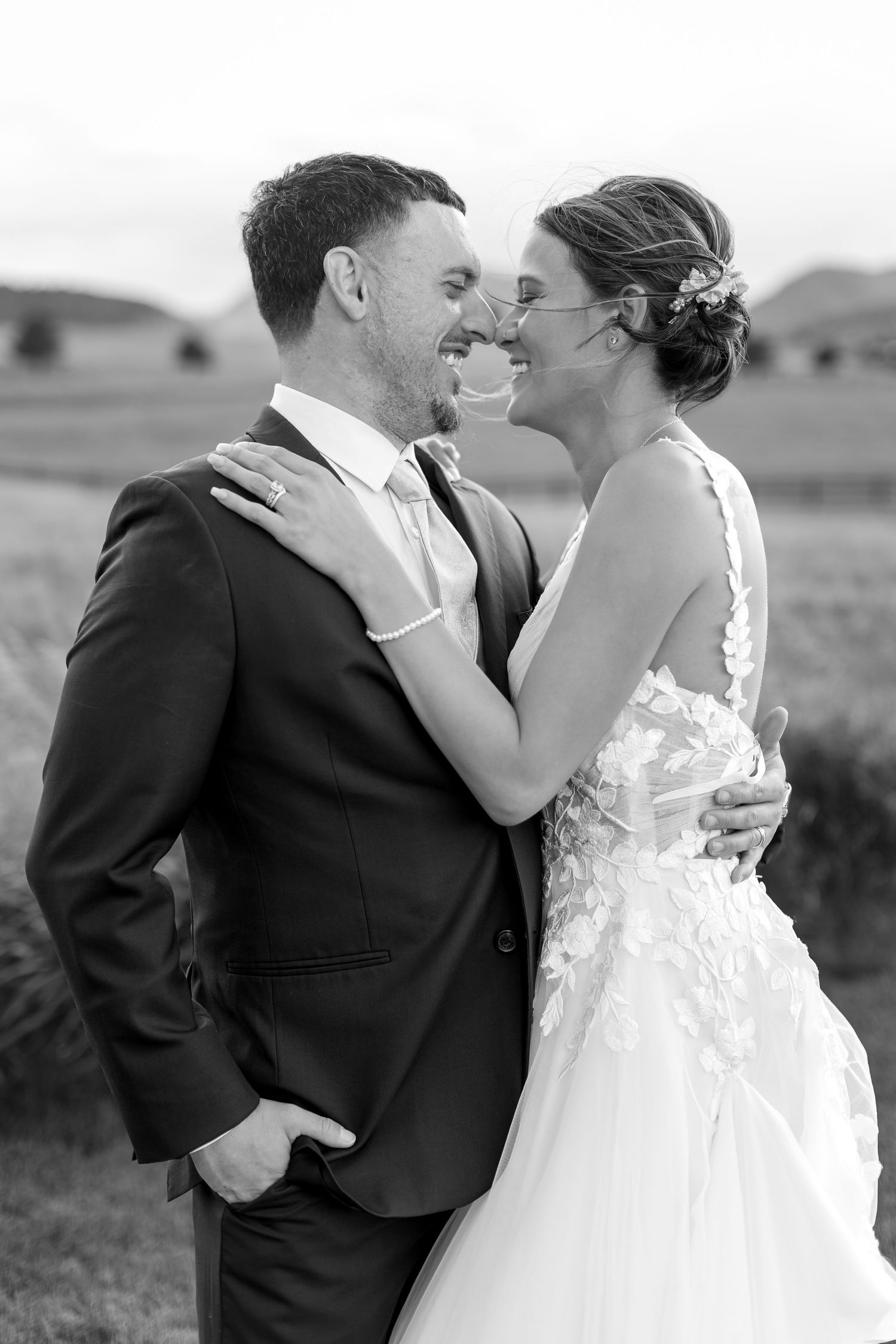 Black and white photo of smiling bride and groom embracing closely in an open field.
