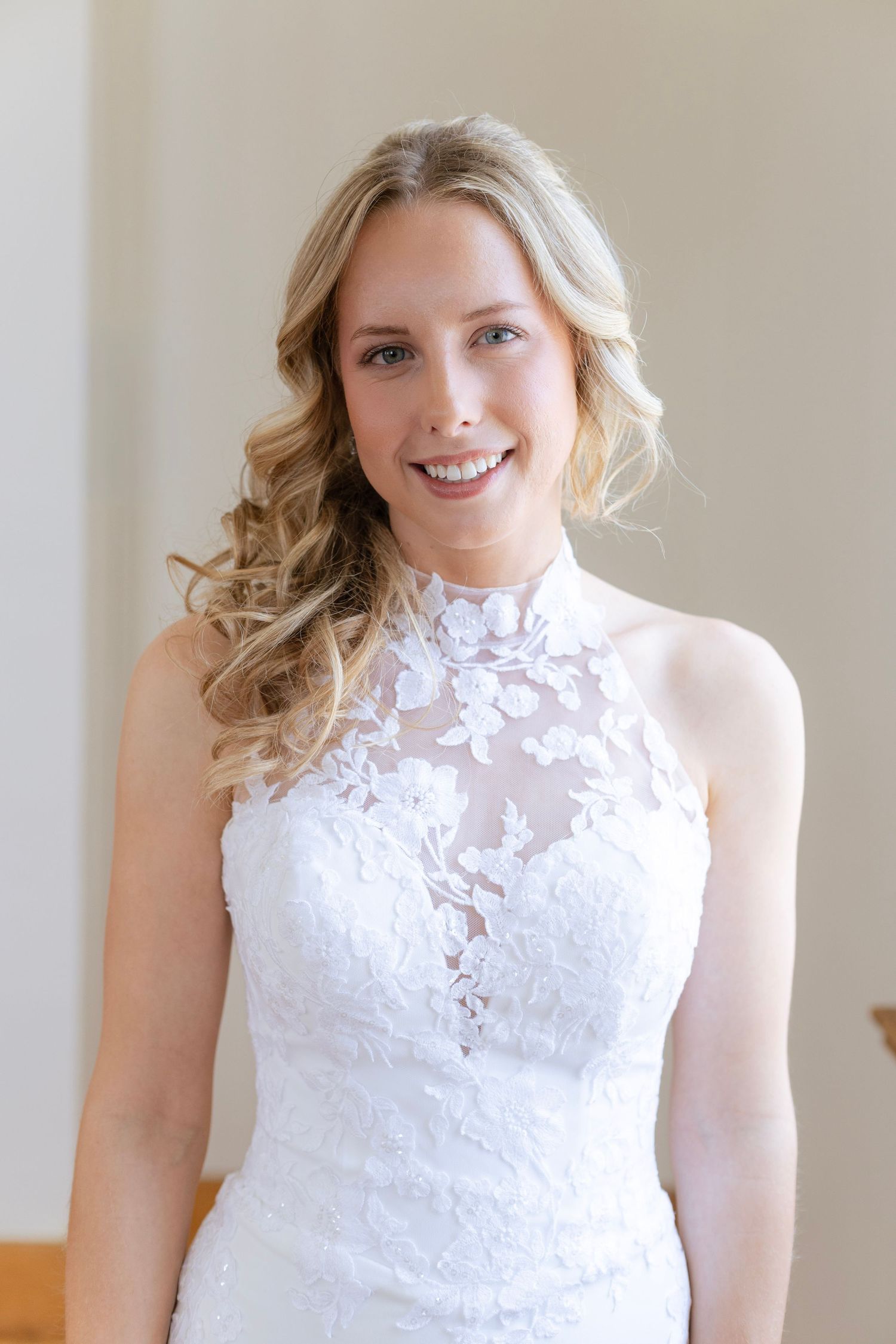 Beautiful blonde bride smiling in a white lace halter wedding gown on her wedding day.