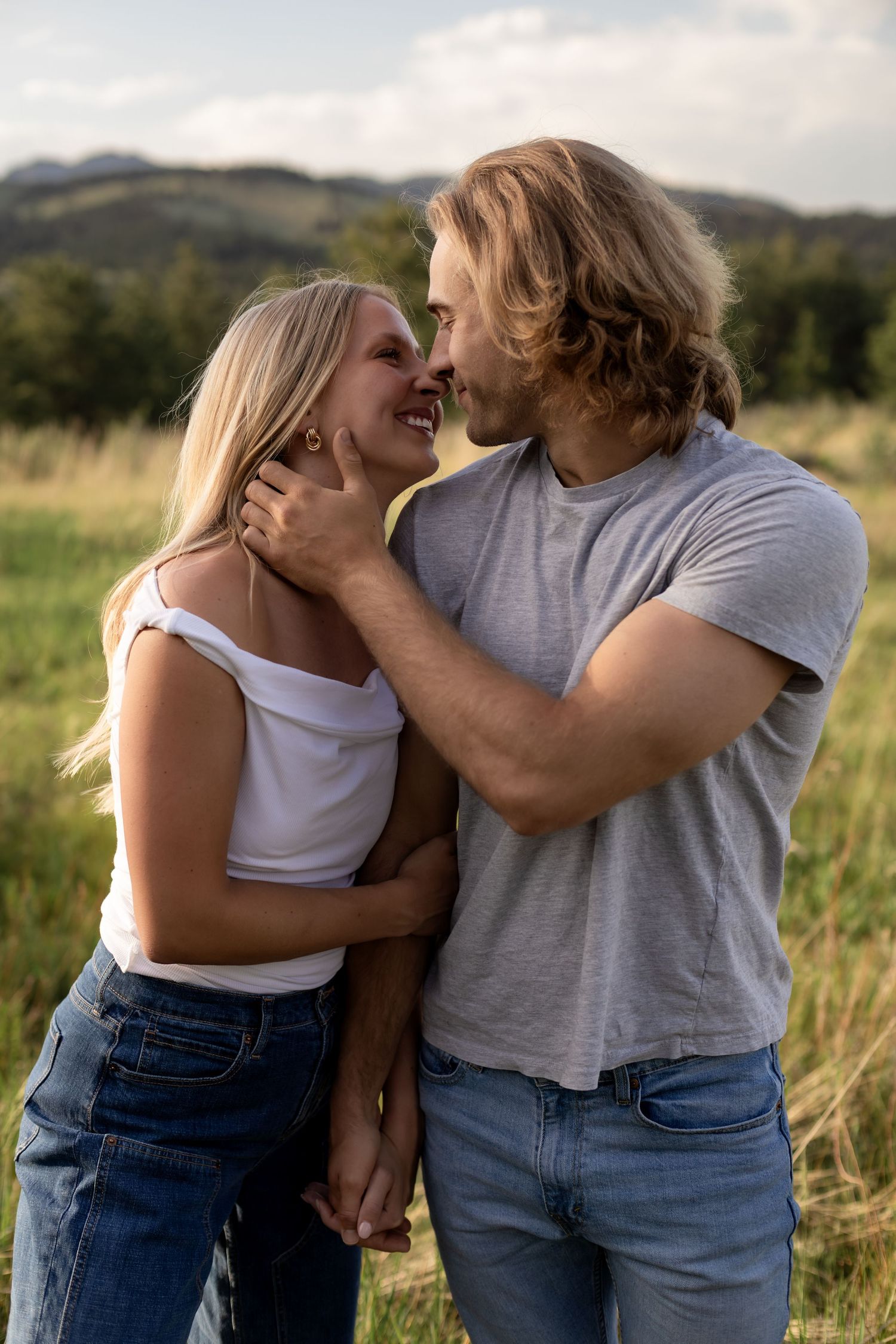 A couple shares a romantic moment in a grassy field, smiling at each other while holding hands outdoors.