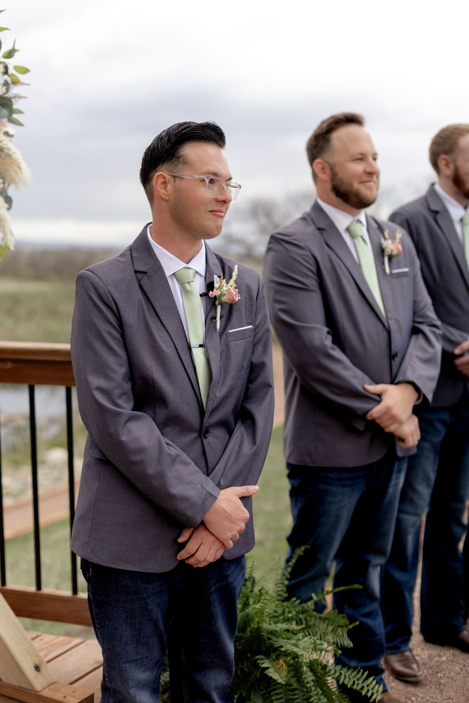 Groom in gray suit with green tie and boutonniere waiting at altar with groomsmen.
