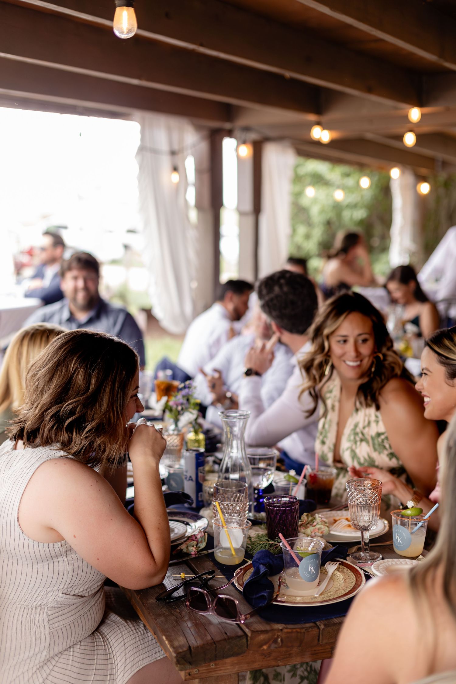 Guests smiling and socializing at an outdoor dining event with string lights and a beautifully set table.