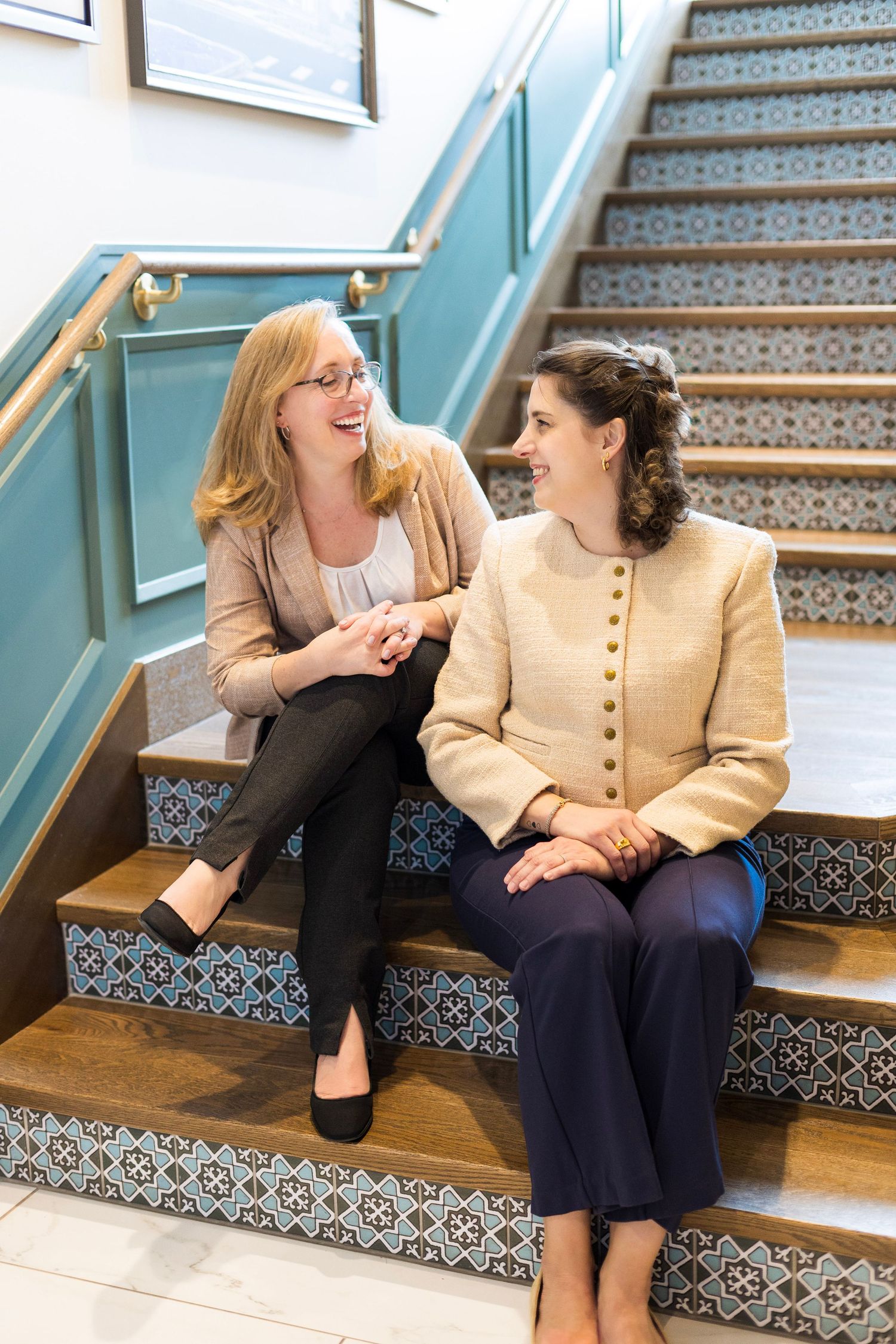 Two colleagues share a lighthearted moment while sitting on decorative stairs with teal railings.