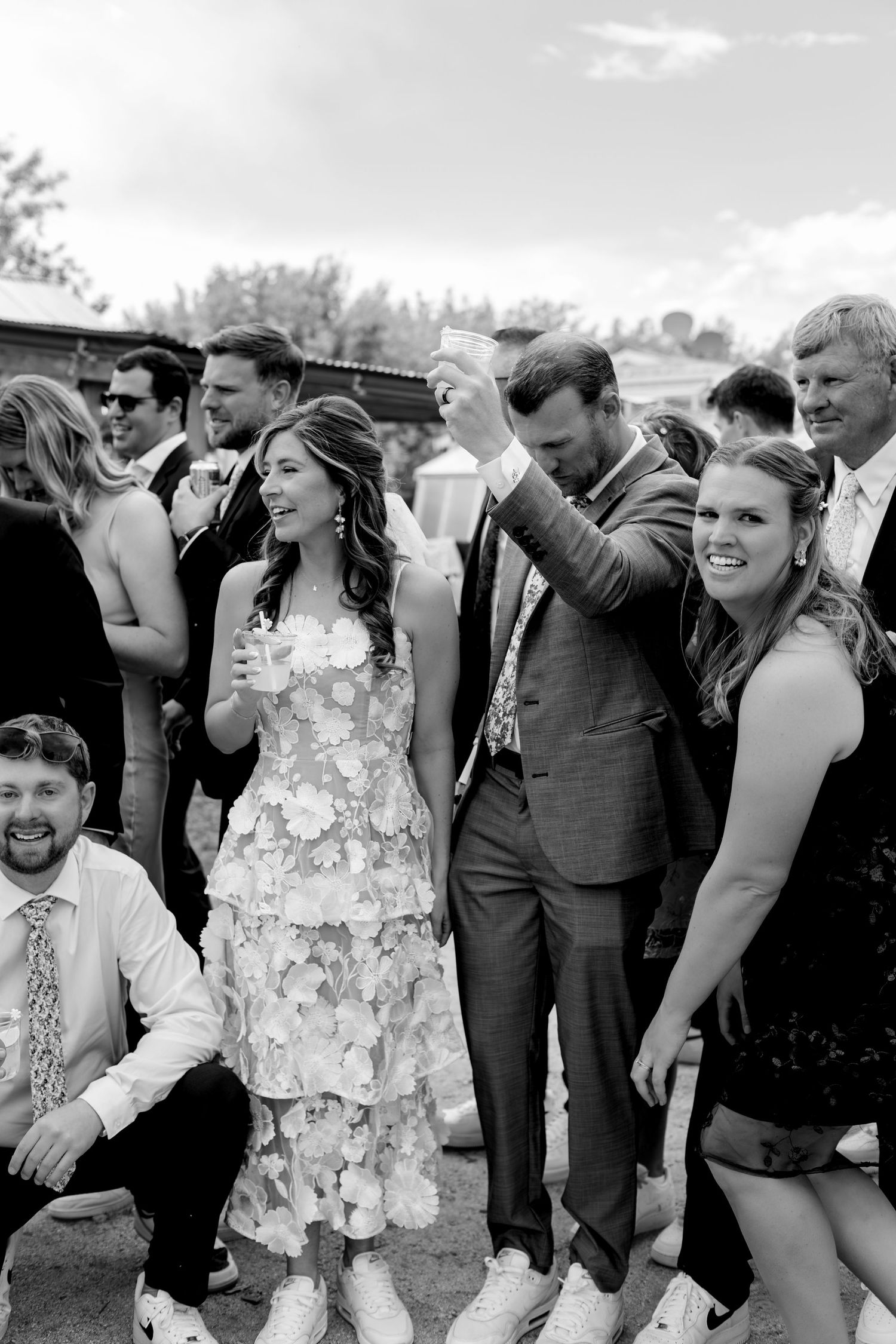 Black and white photo of bride and groom celebrating with wedding guests at an outdoor reception.