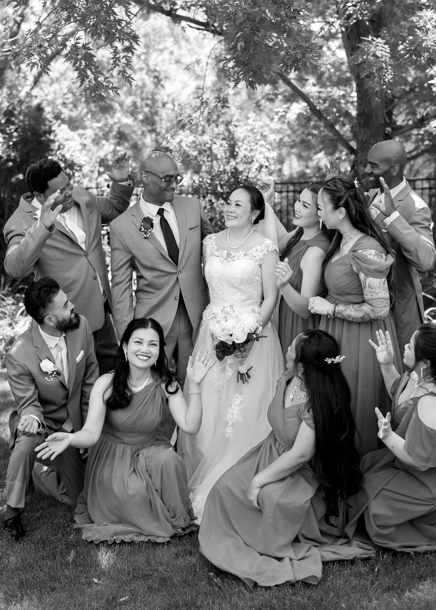 Bride and groom surrounded by joyful wedding party in grey suits and dusty blue dresses.