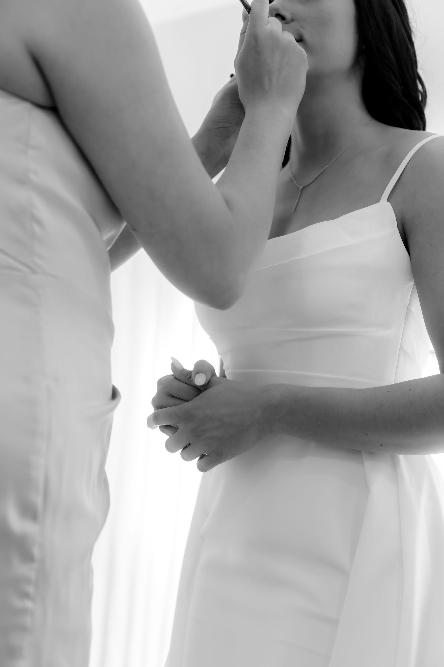 Makeup artist applying lipstick to bride in white slip dress, black and white bridal preparation photo.