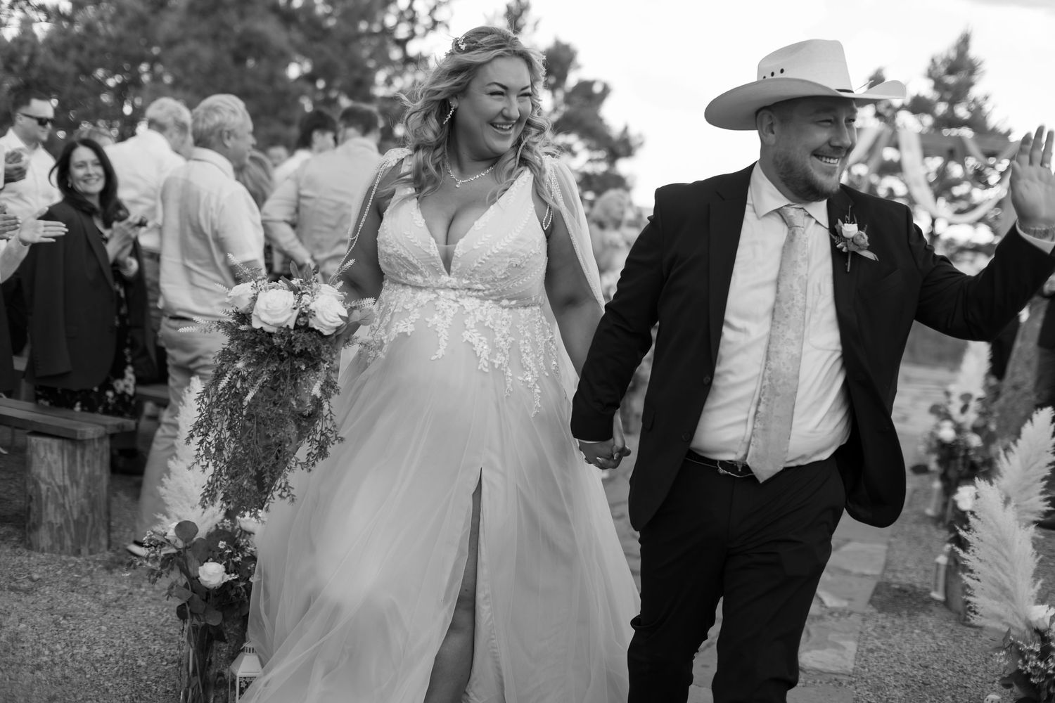 Bride in lace gown and groom in cowboy hat celebrate after outdoor wedding ceremony.