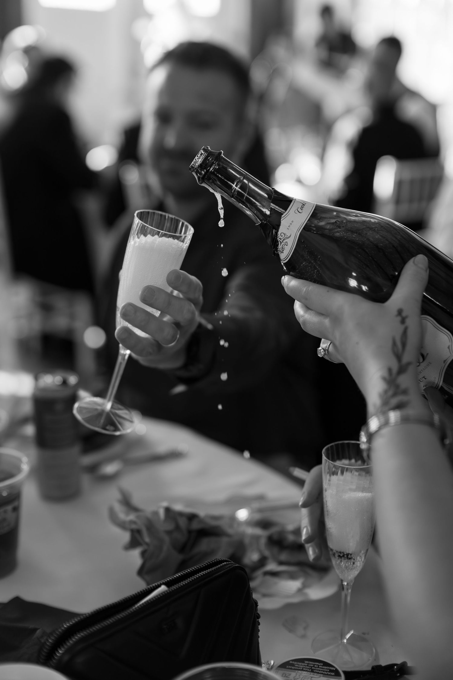 Champagne being poured into a flute glass at a wedding reception in black and white photo.