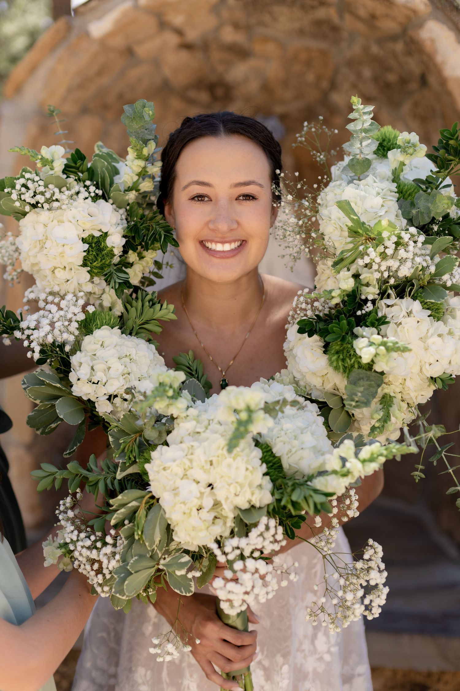Smiling bride holding white hydrangea and greenery bouquets on her wedding day.