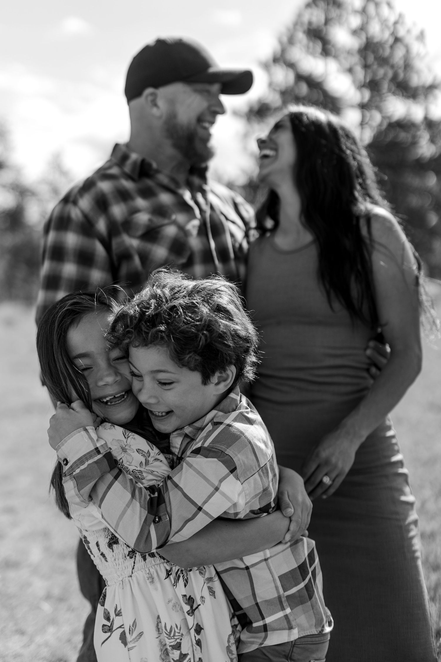 Black and white family photo of parents laughing while two children hug joyfully outdoors.