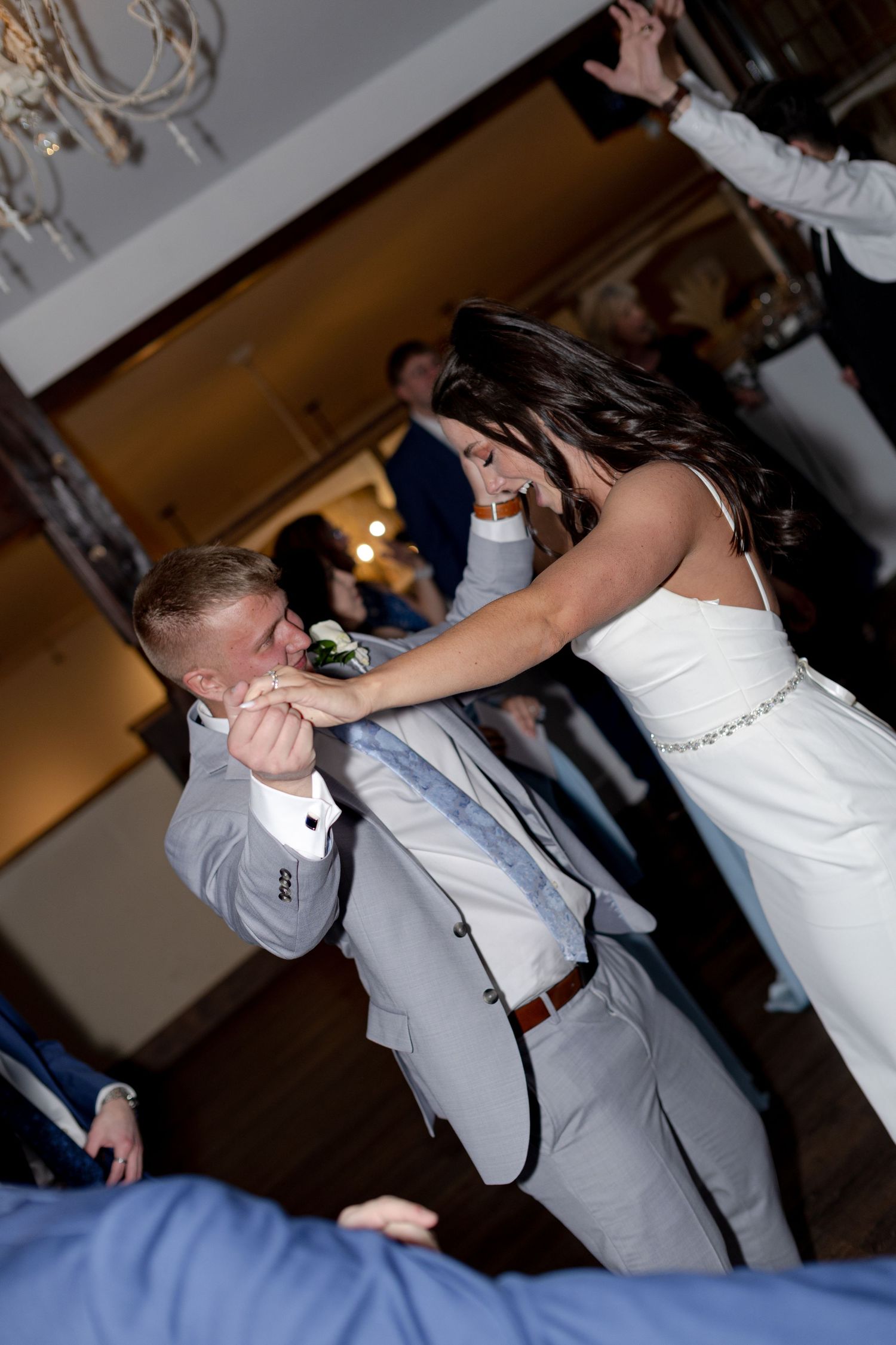 Bride and groom dance energetically at wedding reception, with groom kissing bride's hand on the dance floor.