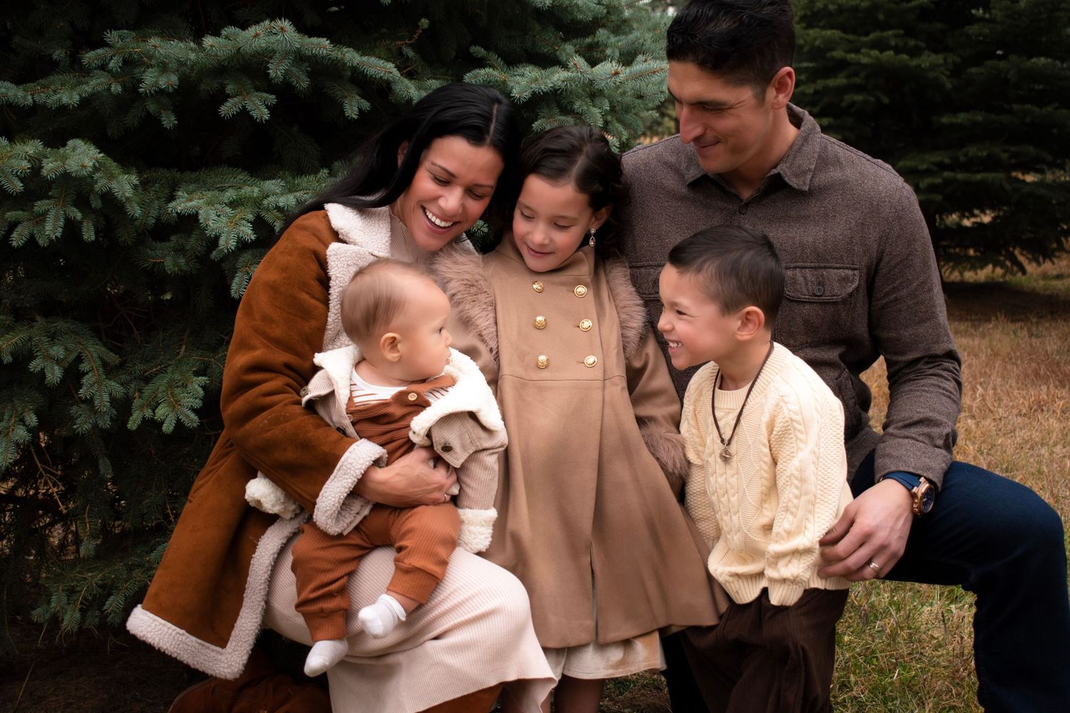 Family portrait session outdoors with evergreen trees in the background.