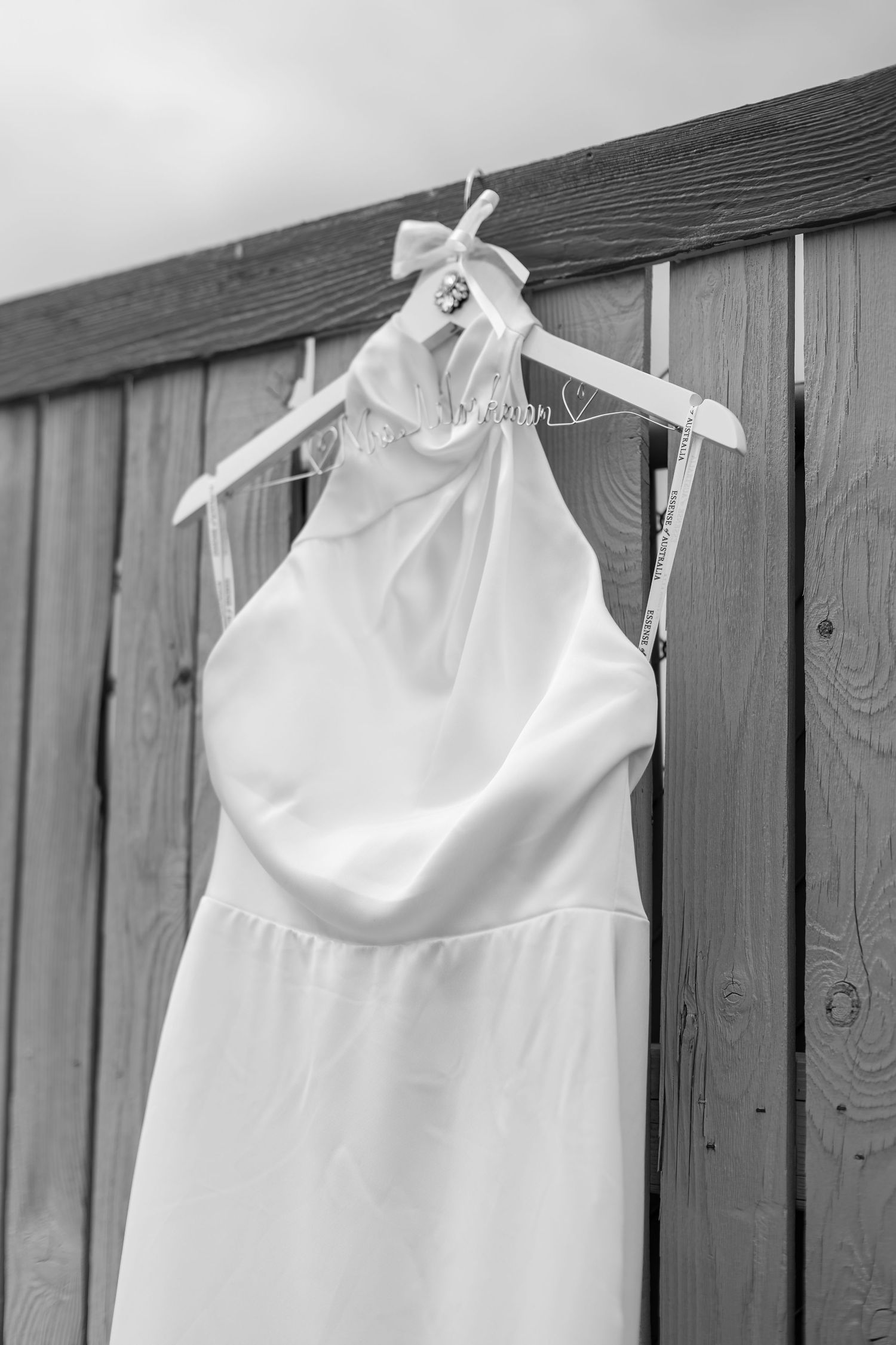 Black and white photo of a minimalist halter-neck wedding dress hanging on a wooden fence.