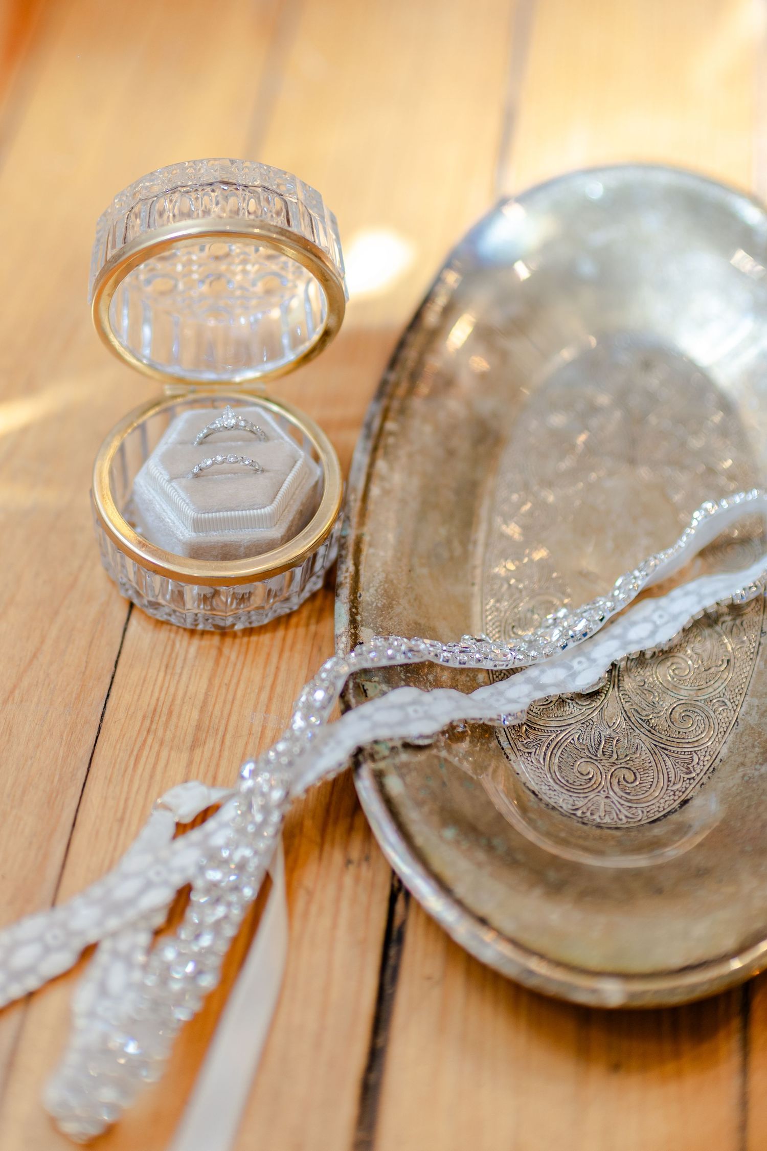 Elegant wedding ring box with crystal details beside a silver tray and beaded bridal accessory on wooden surface.