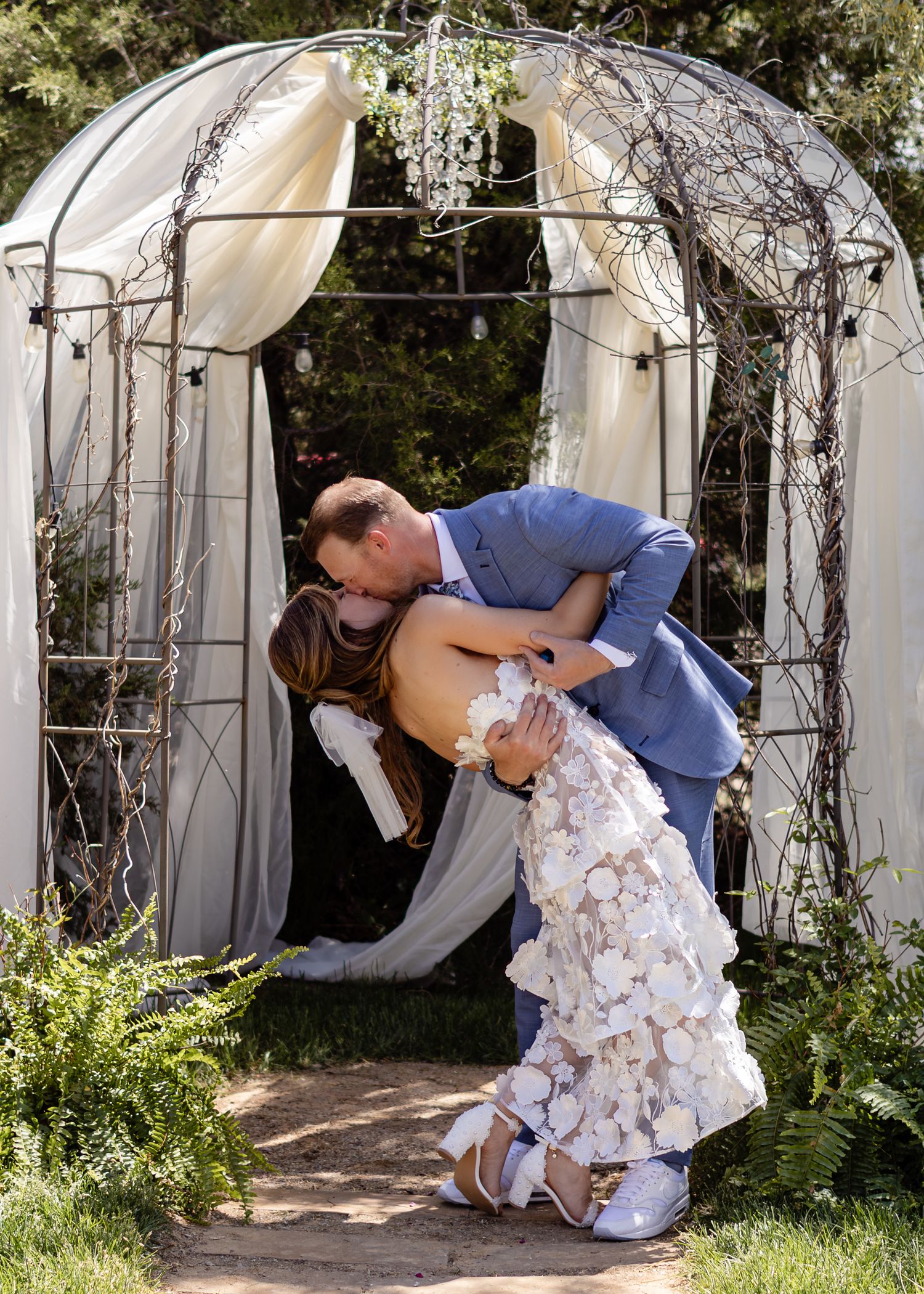 Bride and groom share a romantic dip kiss under a decorated arch at an outdoor wedding ceremony.