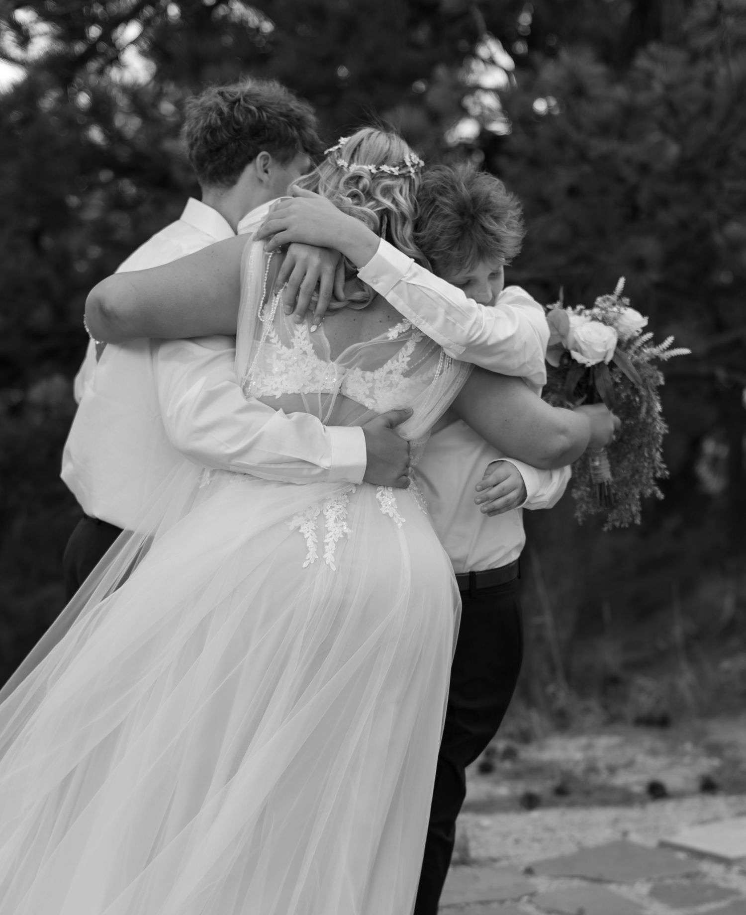 Black and white photo of bride and groom sharing a group hug with guests at an outdoor wedding ceremony.