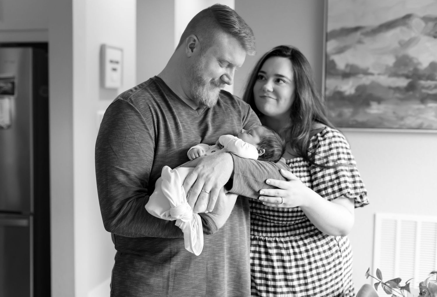 Black and white photo of a couple tenderly holding their newborn baby at home.