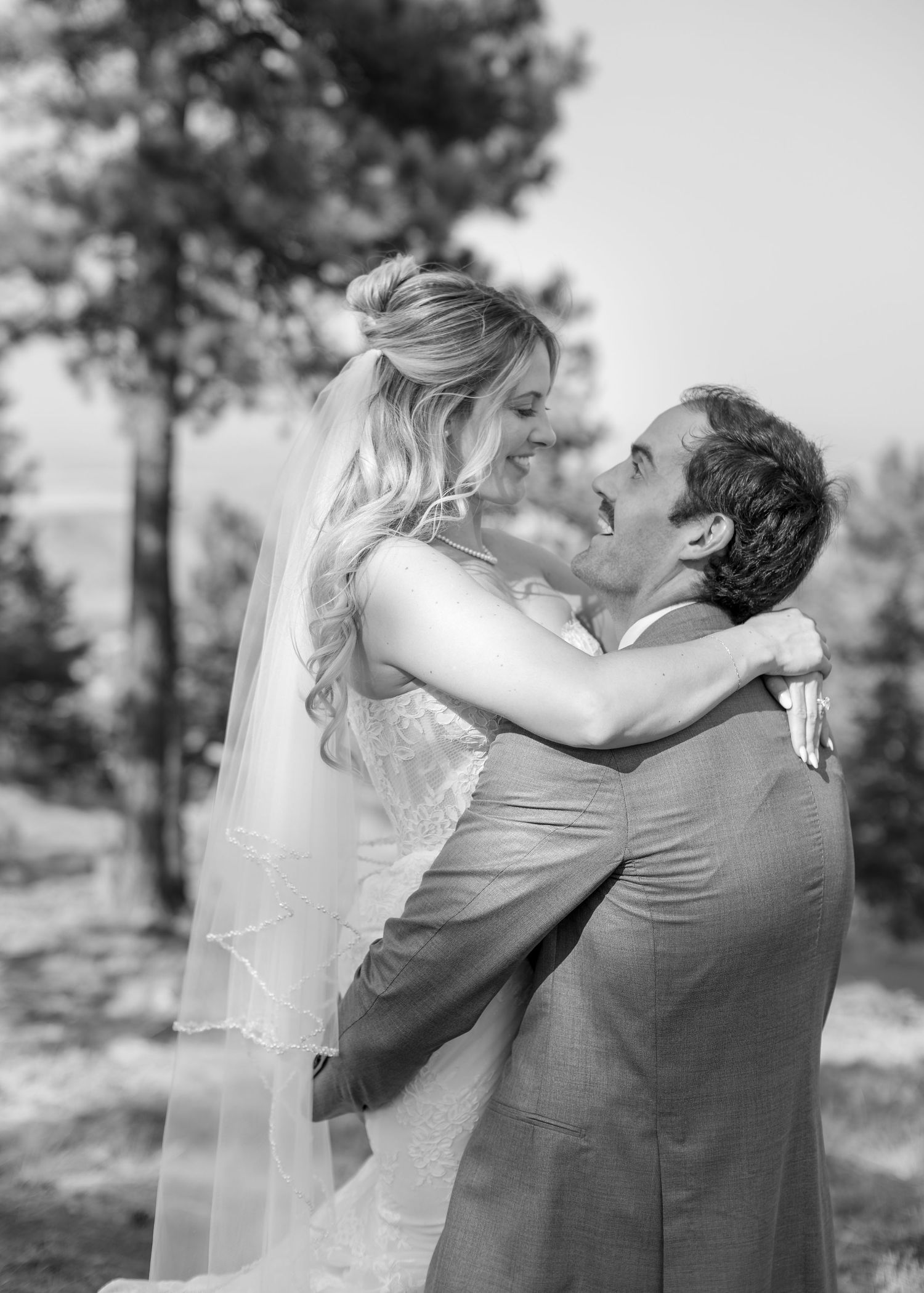 Black and white photo of a groom lifting his bride in a joyful embrace outdoors on their wedding day.