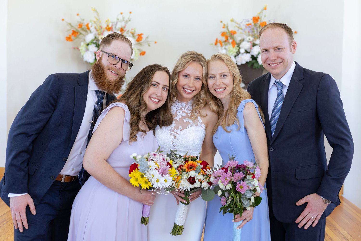 Bride with bridesmaids in blue dresses and groomsmen in navy suits posing at a wedding ceremony.