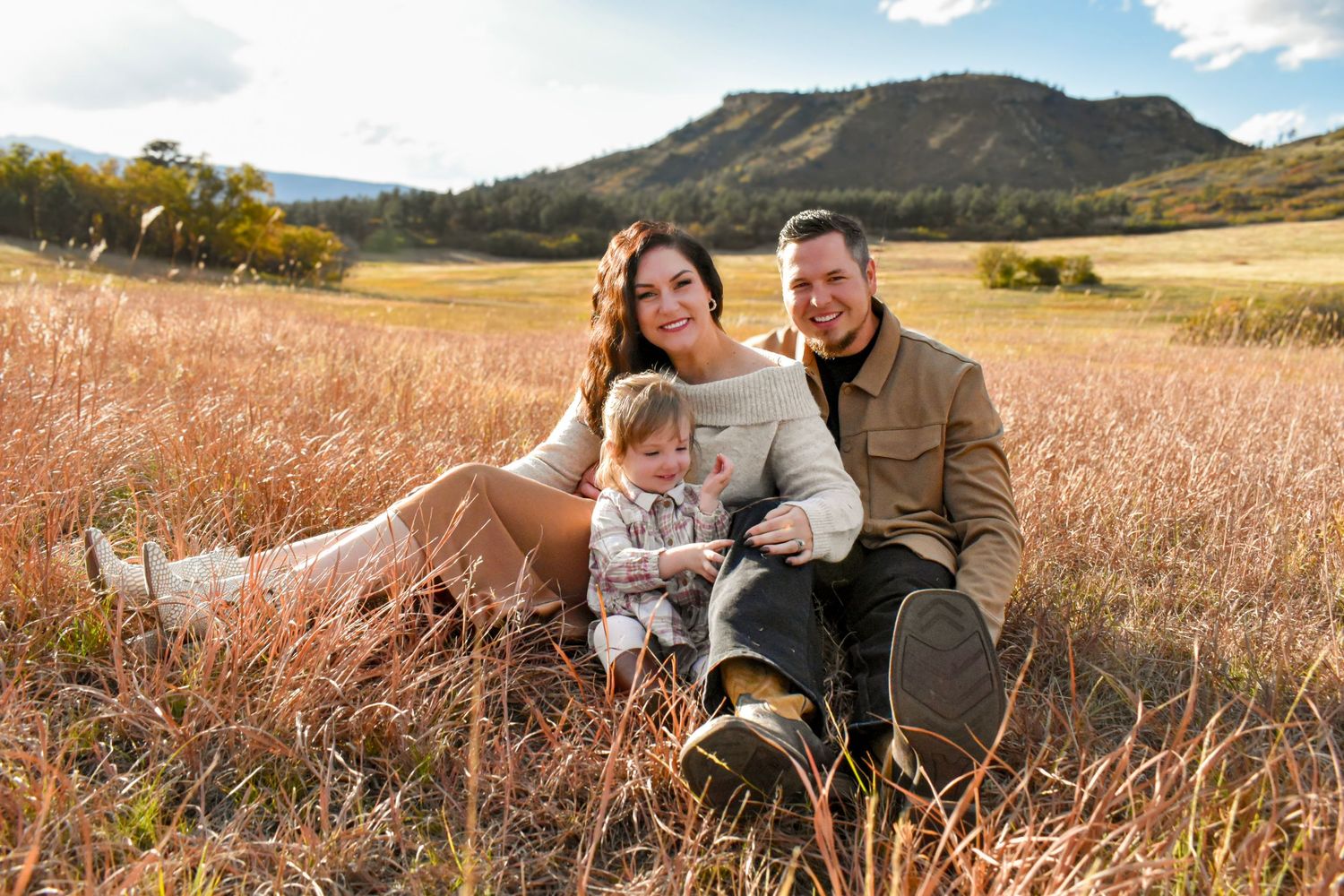 A couple relaxes together in a scenic mountain field during golden hour.