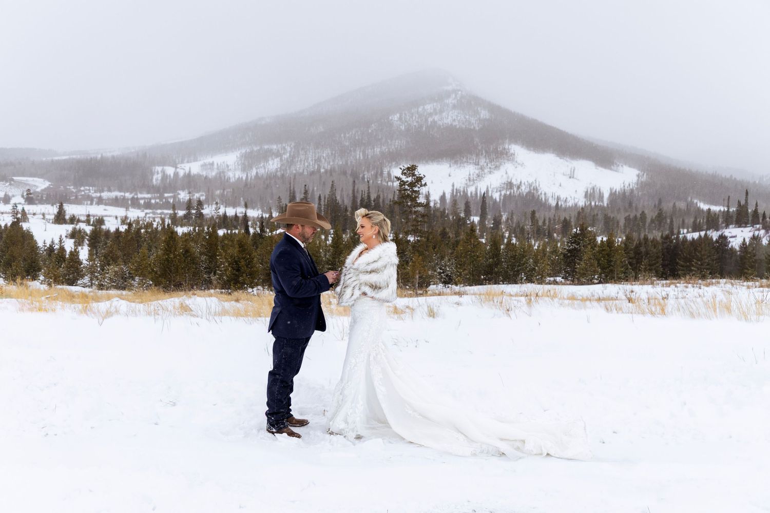 A winter wedding celebration takes place in a snowy mountain landscape with snow-covered peaks in the background.