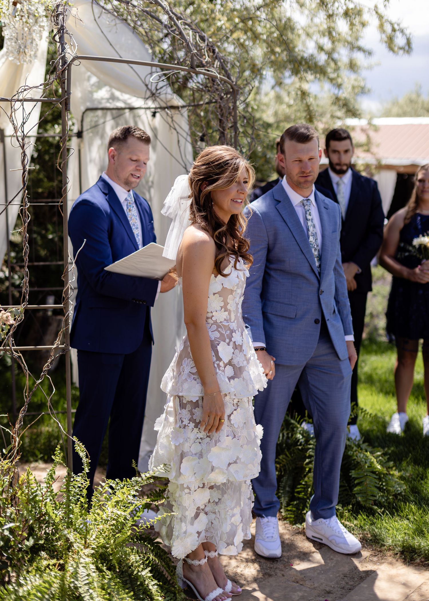 Bride and groom stand at outdoor wedding altar with officiant reading ceremony vows.