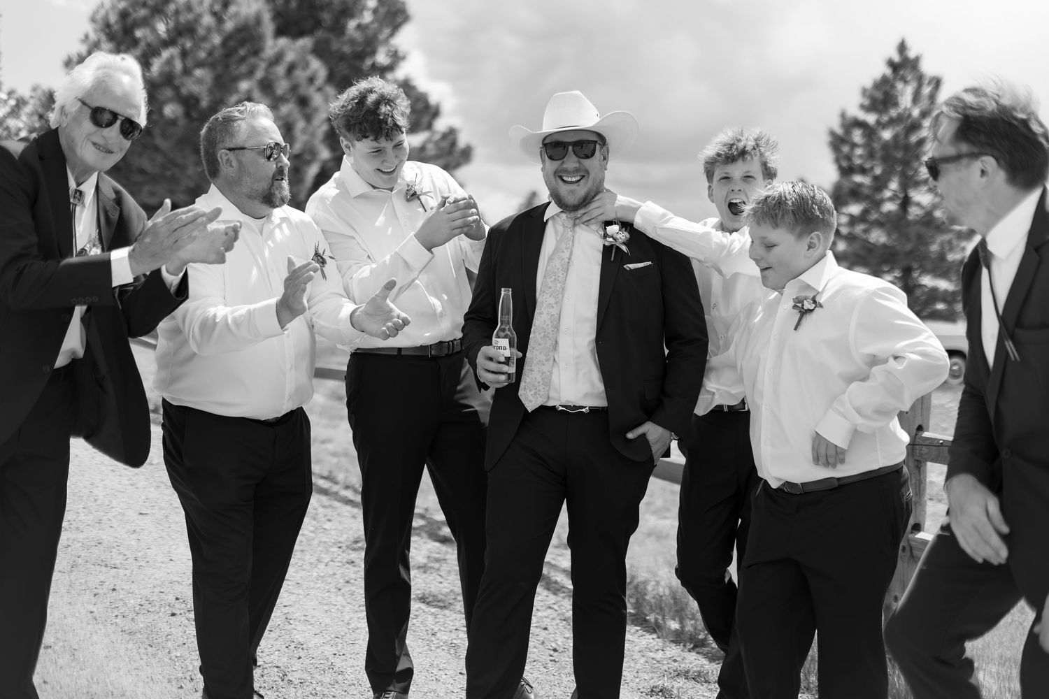 Black and white photo of groom with groomsmen laughing outdoors at wedding celebration.