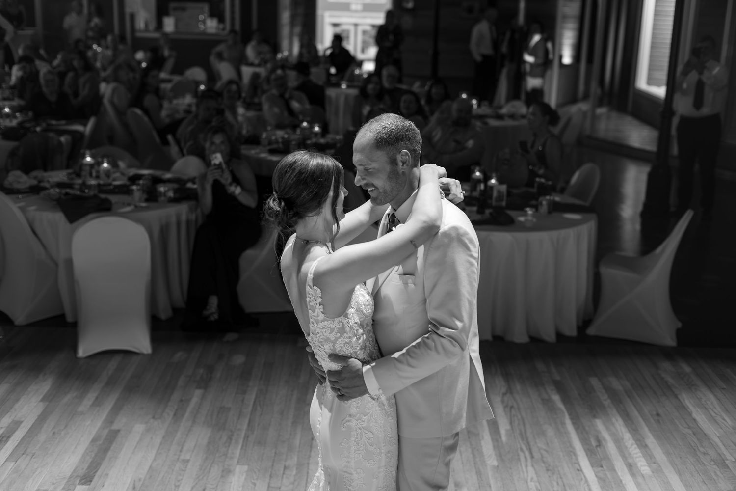 Black and white photo of a bride and groom sharing their first dance at a wedding reception.