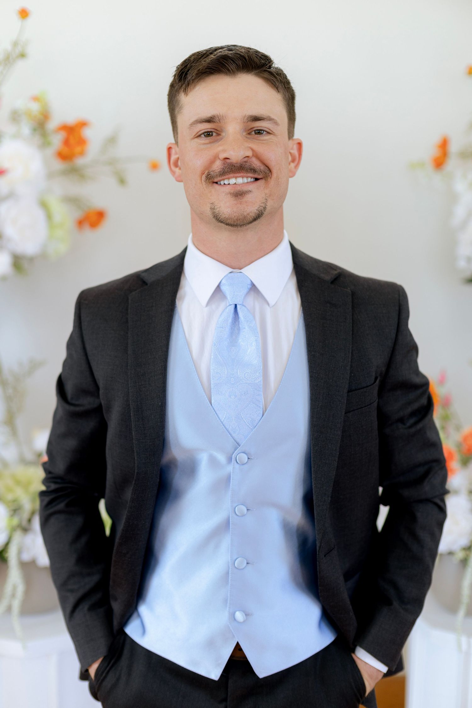 Handsome groom smiling in a black suit with light blue vest and tie at his wedding.