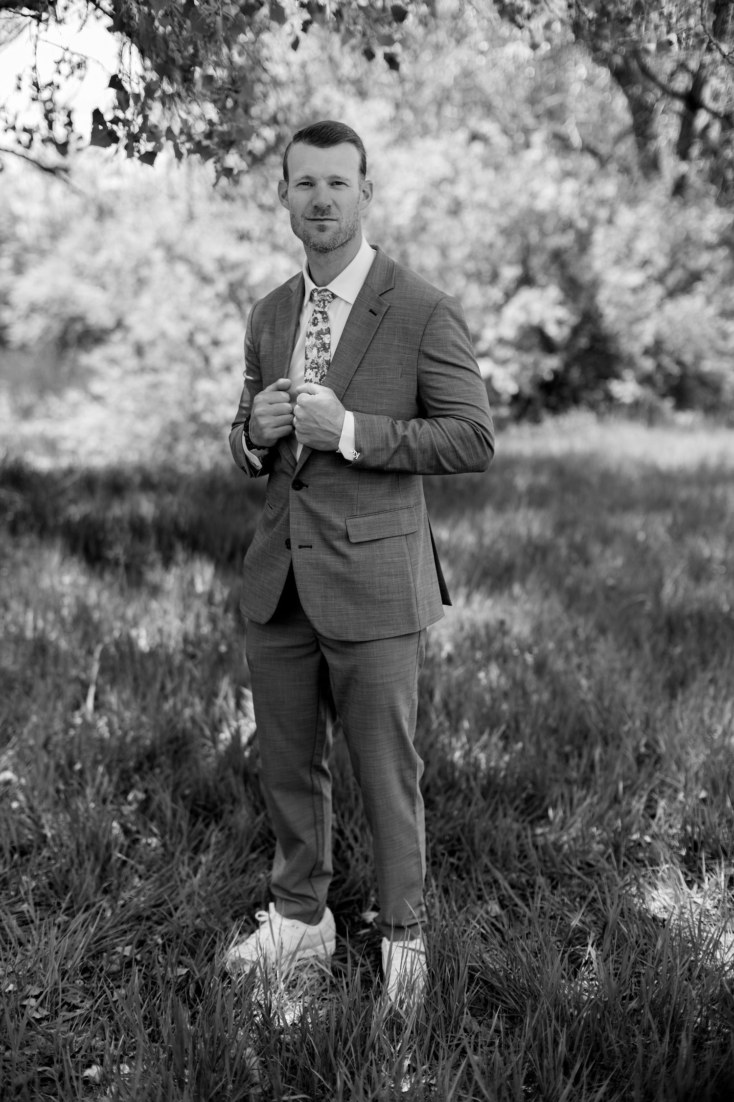 Elegant groom in a plaid suit poses confidently outdoors in black and white wedding portrait.