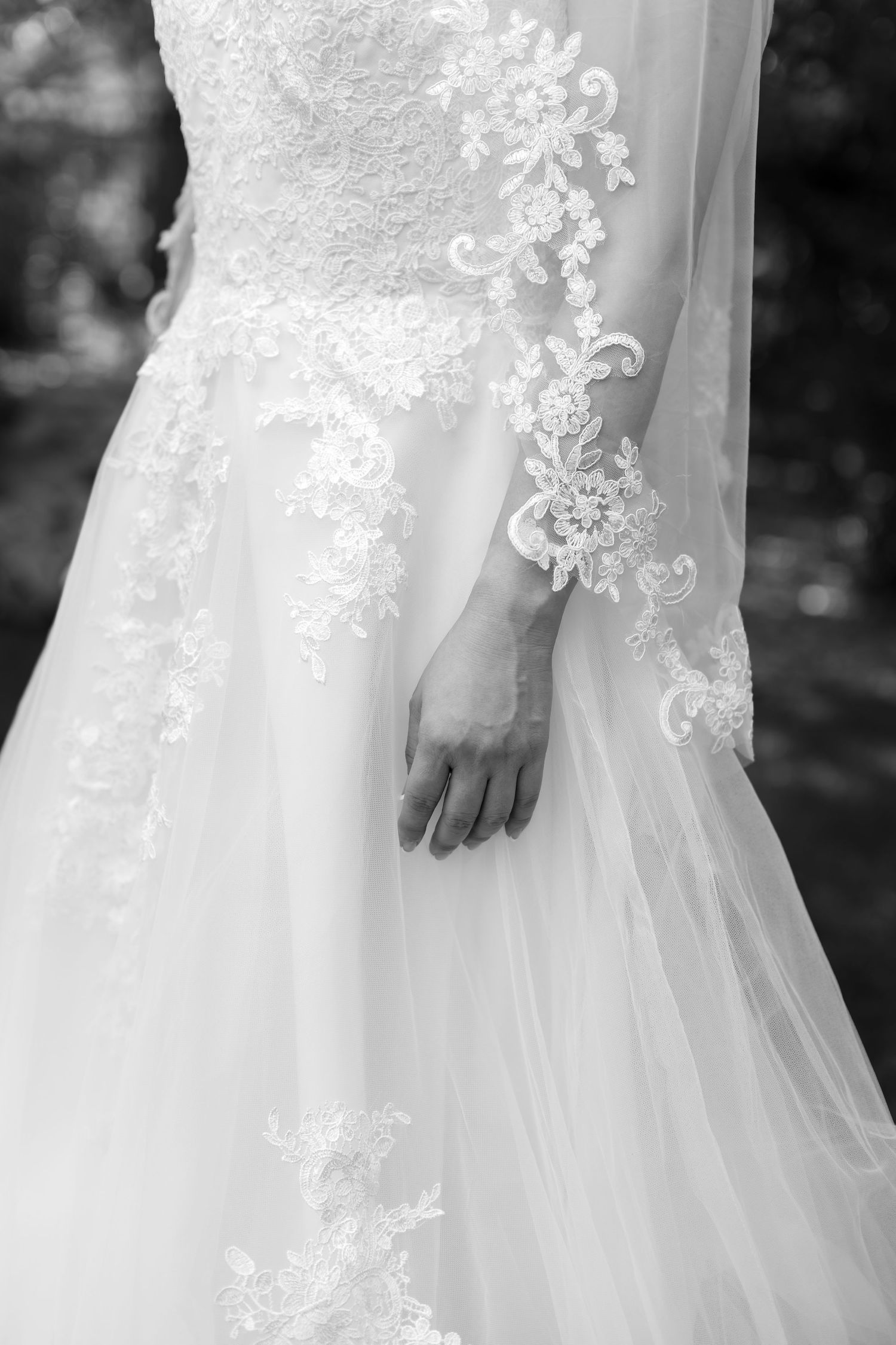 Close-up black and white photo of a bride in a lace long-sleeve wedding gown with floral embroidery details.