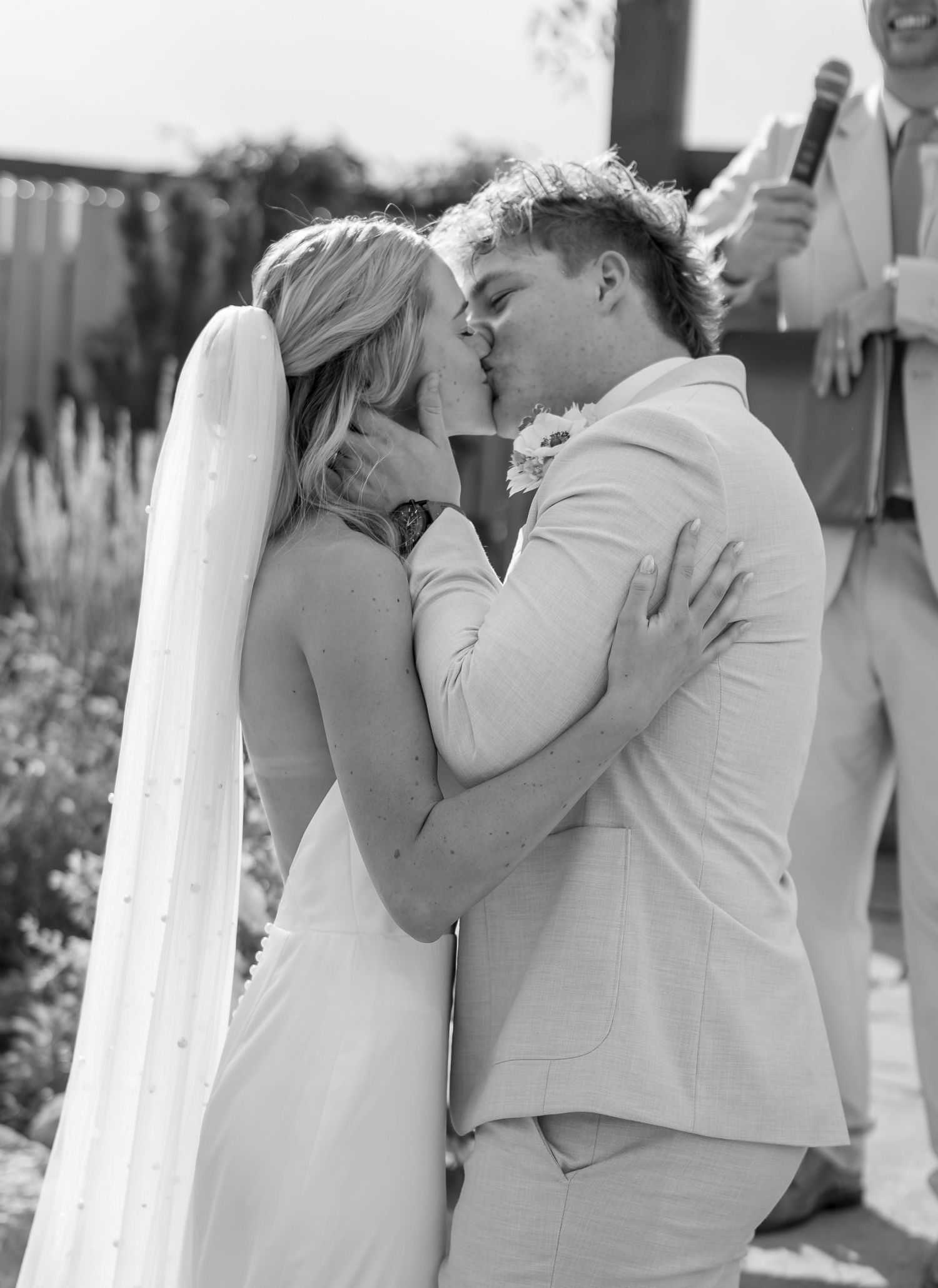 Black and white photo of bride and groom sharing their first kiss at the wedding ceremony altar.