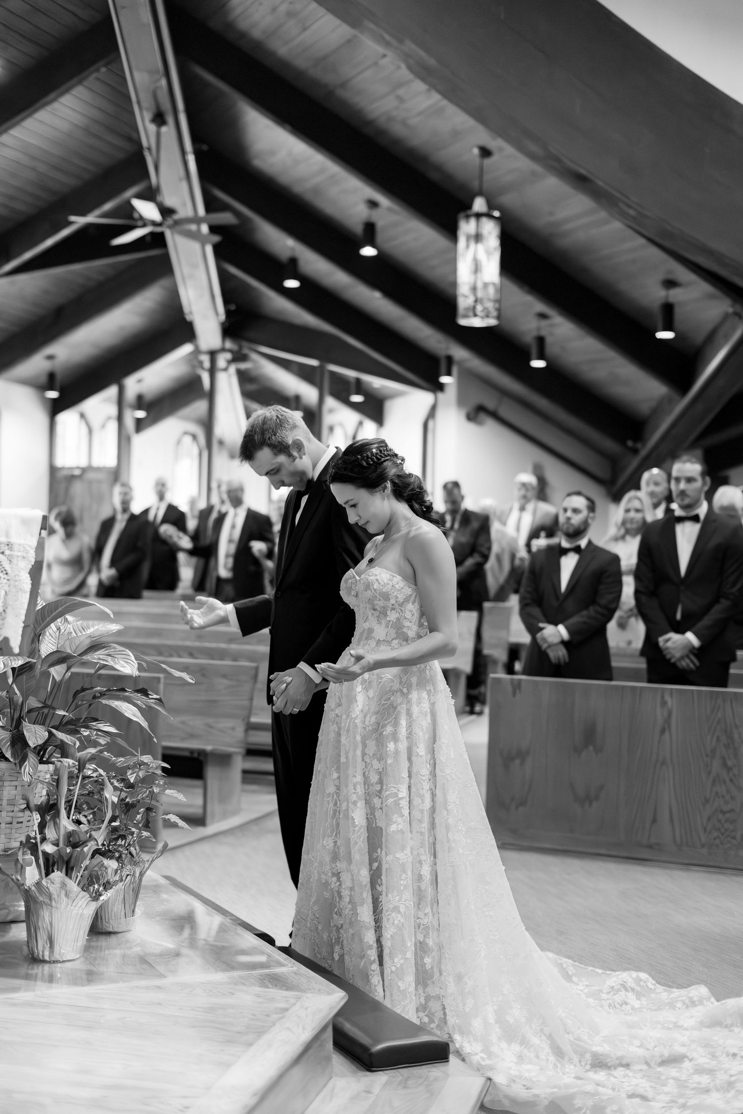 Black and white photo of bride and groom praying together at church altar during elegant wedding ceremony.