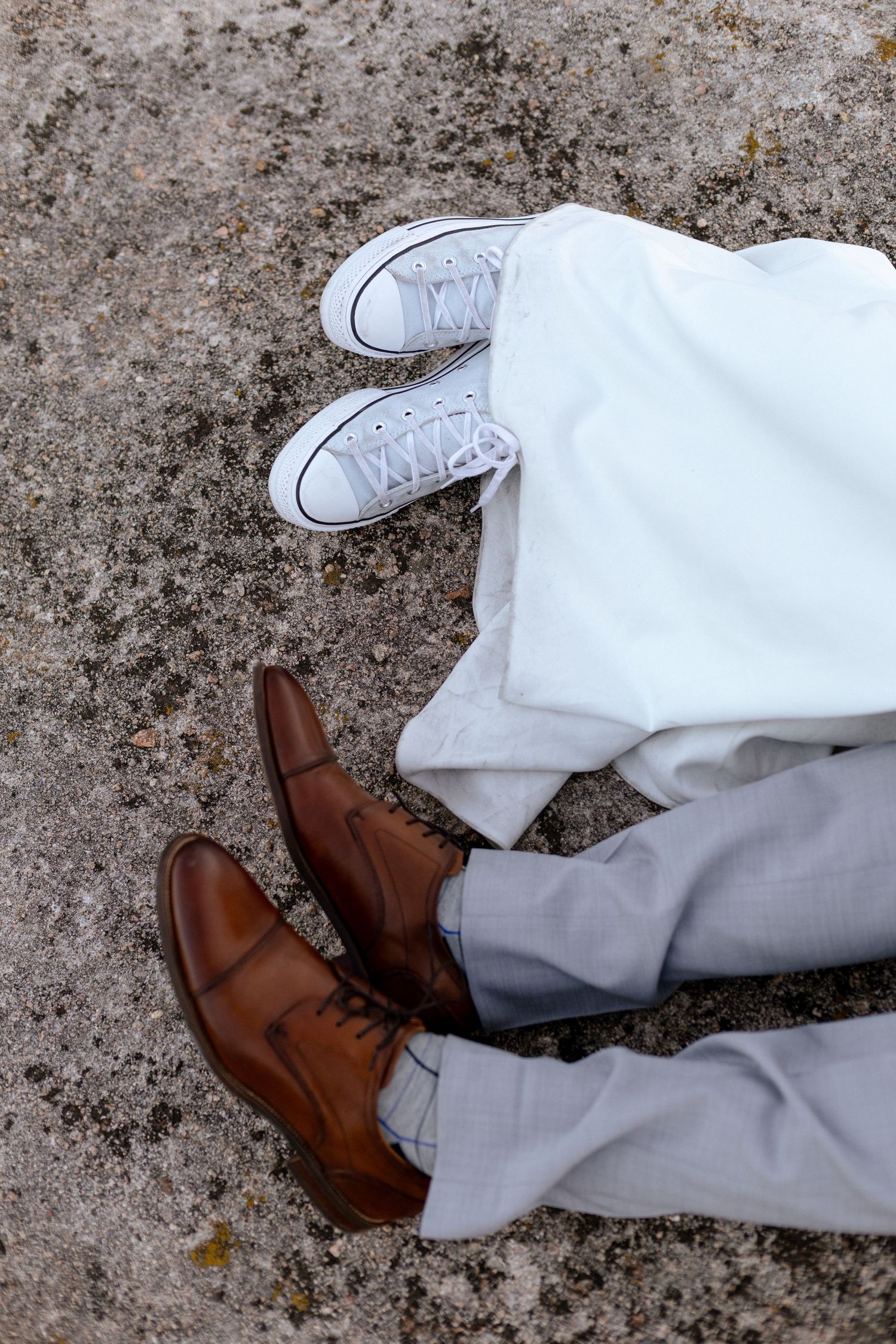 Wedding couple feet showing white sneakers and brown leather dress shoes.
