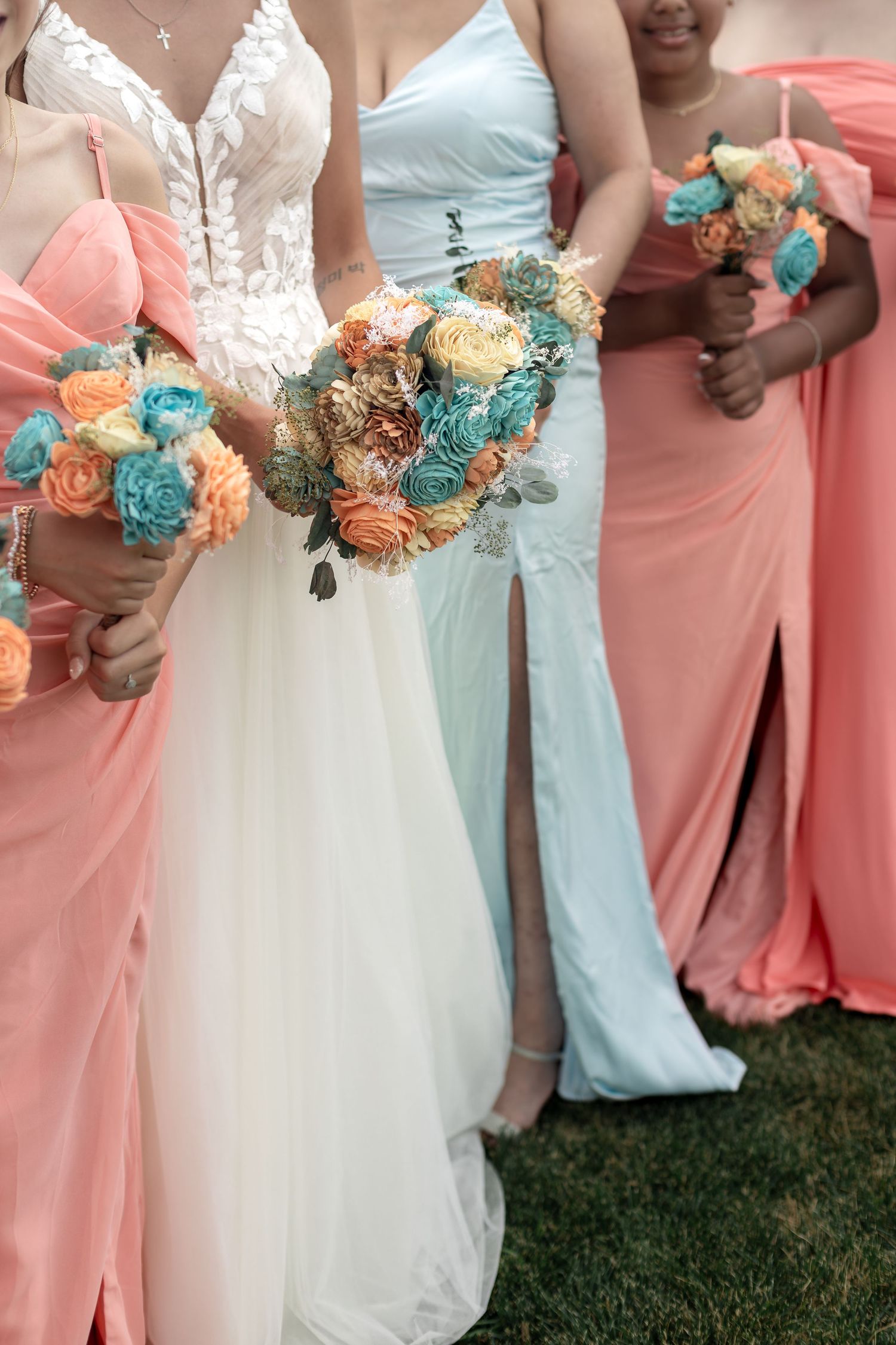 Bride in white gown with bridesmaids in coral and blue holding colorful floral bouquets.