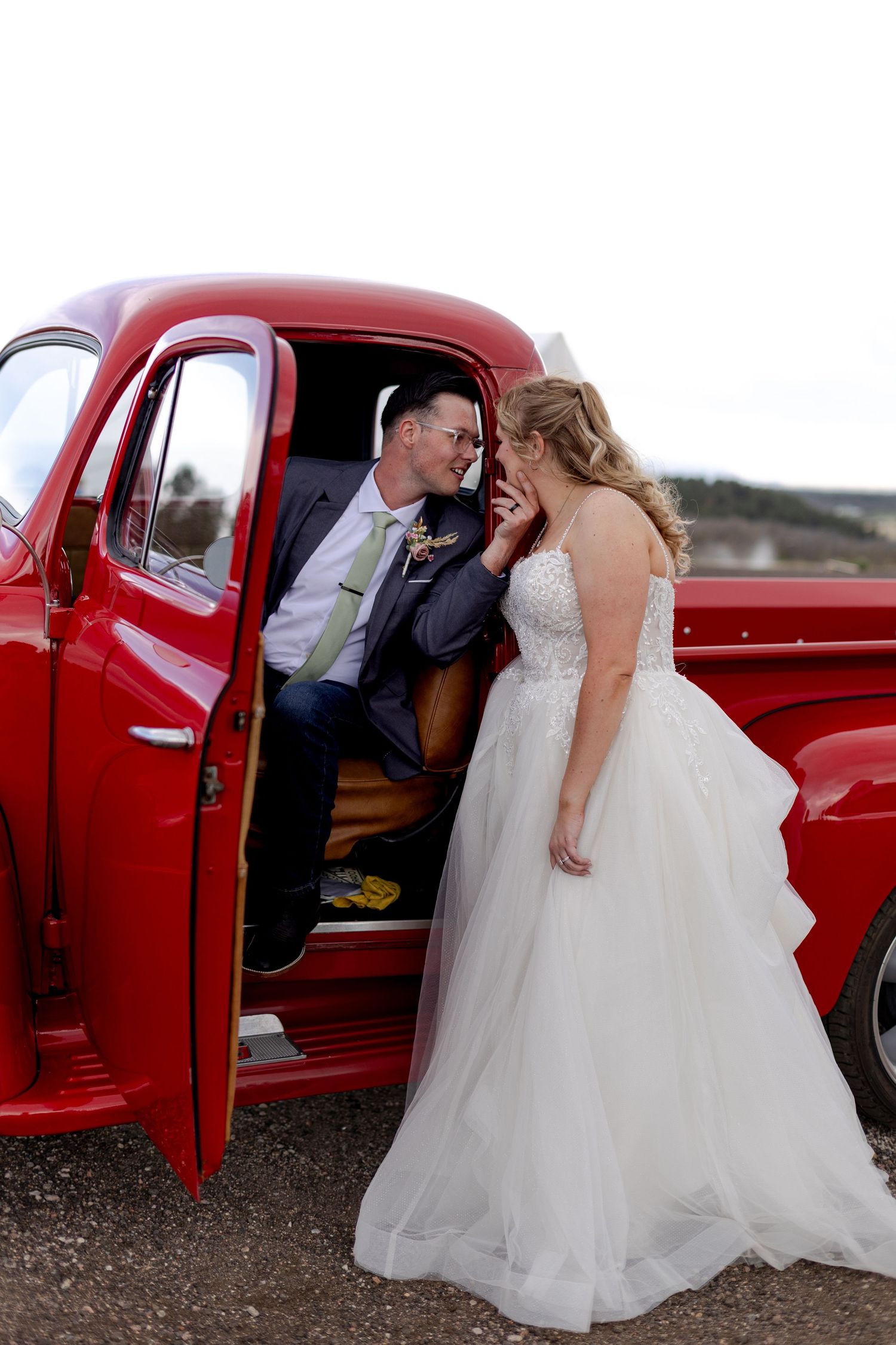 Bride and groom share a romantic moment by a classic red vintage truck on their wedding day.