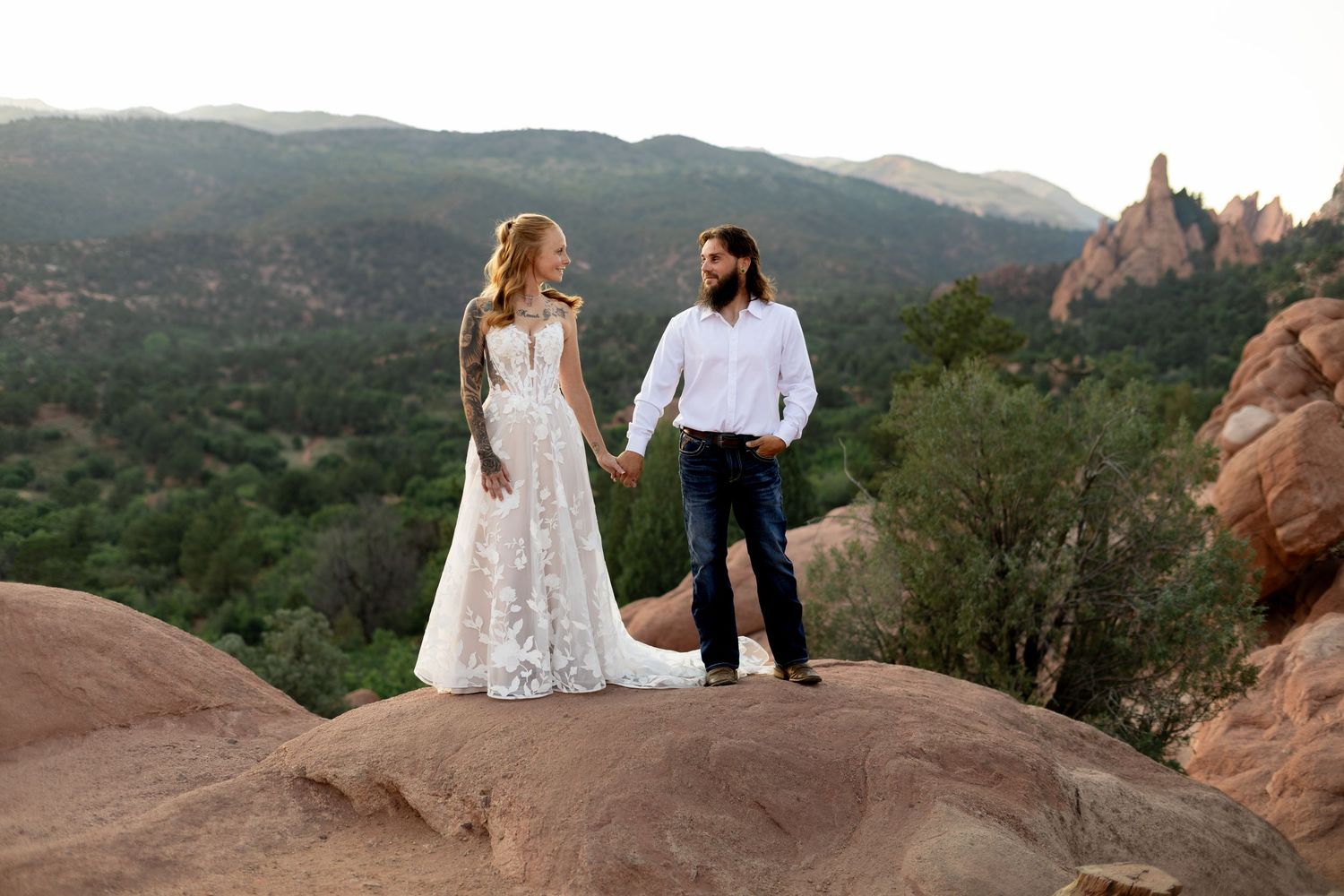Bride and groom hold hands on red rocks at Garden of the Gods with mountain backdrop.