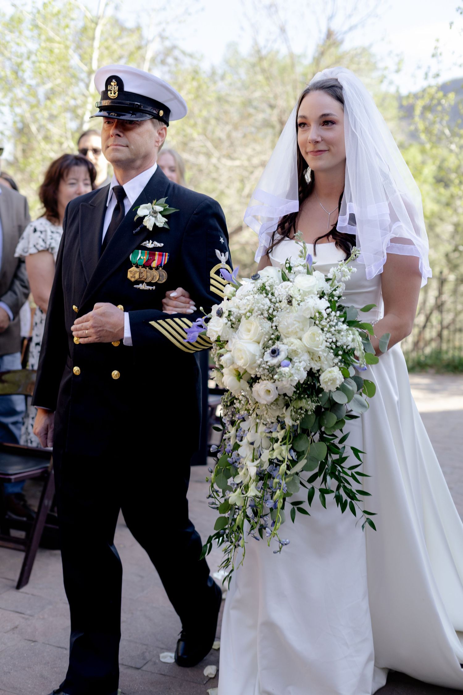 Navy officer escorts bride down the aisle at outdoor wedding ceremony.