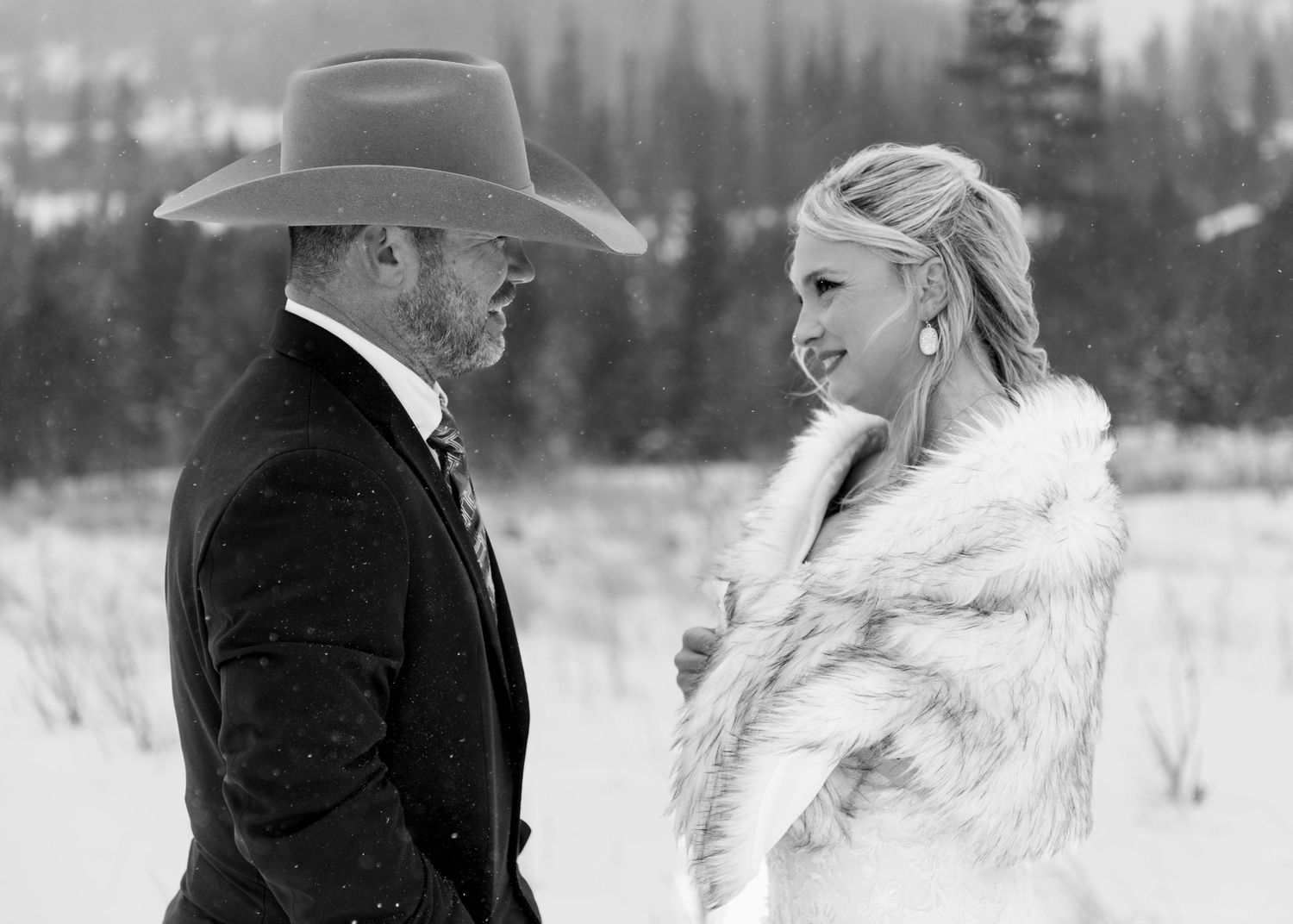 A black and white photo of a couple in winter wedding attire, with the groom in a cowboy hat and the bride in a fur wrap.