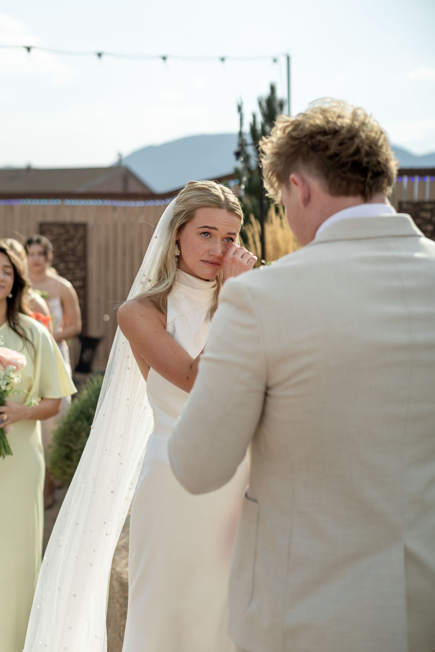 Emotional bride wiping tears during outdoor wedding ceremony with groom.