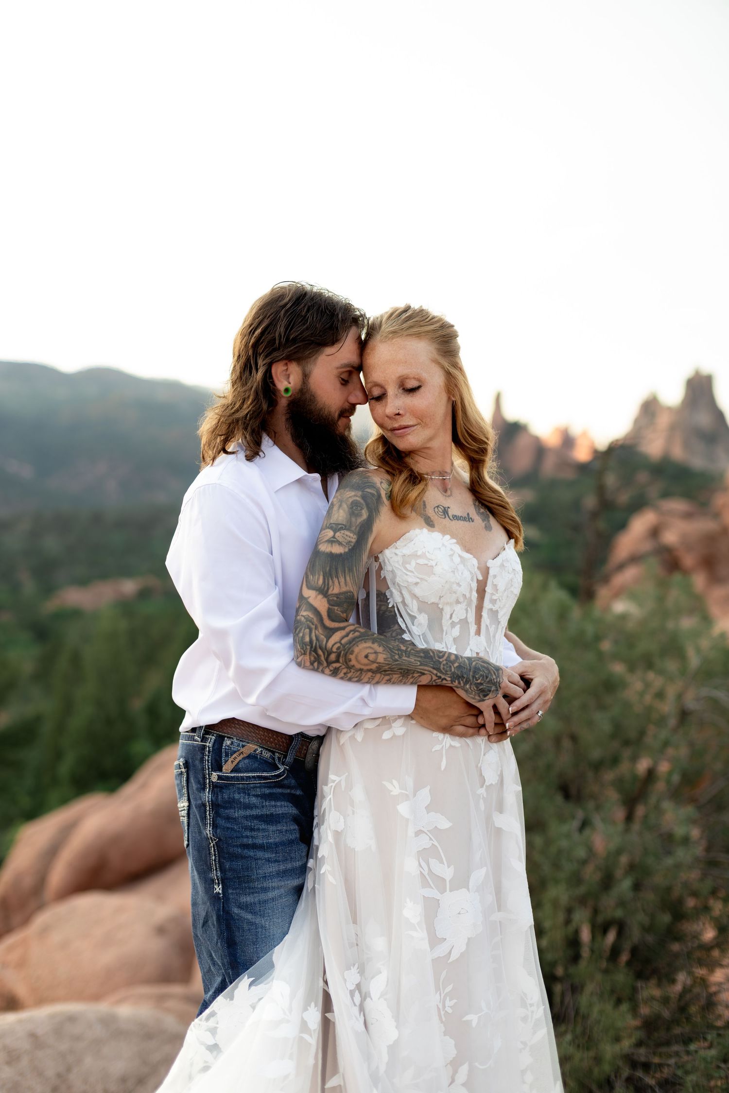 Tattooed groom embraces bride in lace wedding dress at Garden of the Gods, Colorado.