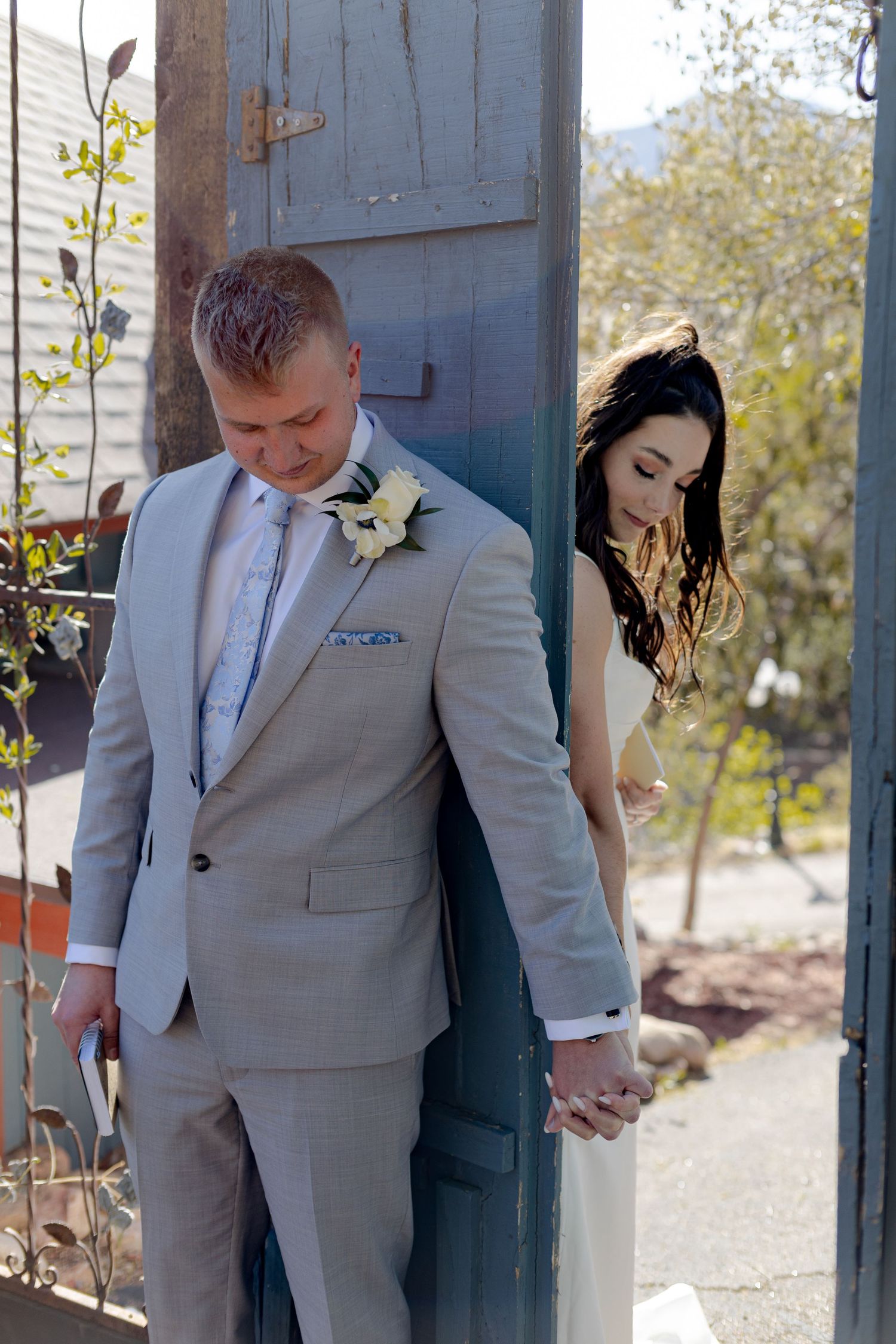 Bride and groom share a tender moment holding hands by a rustic blue door on their wedding day.