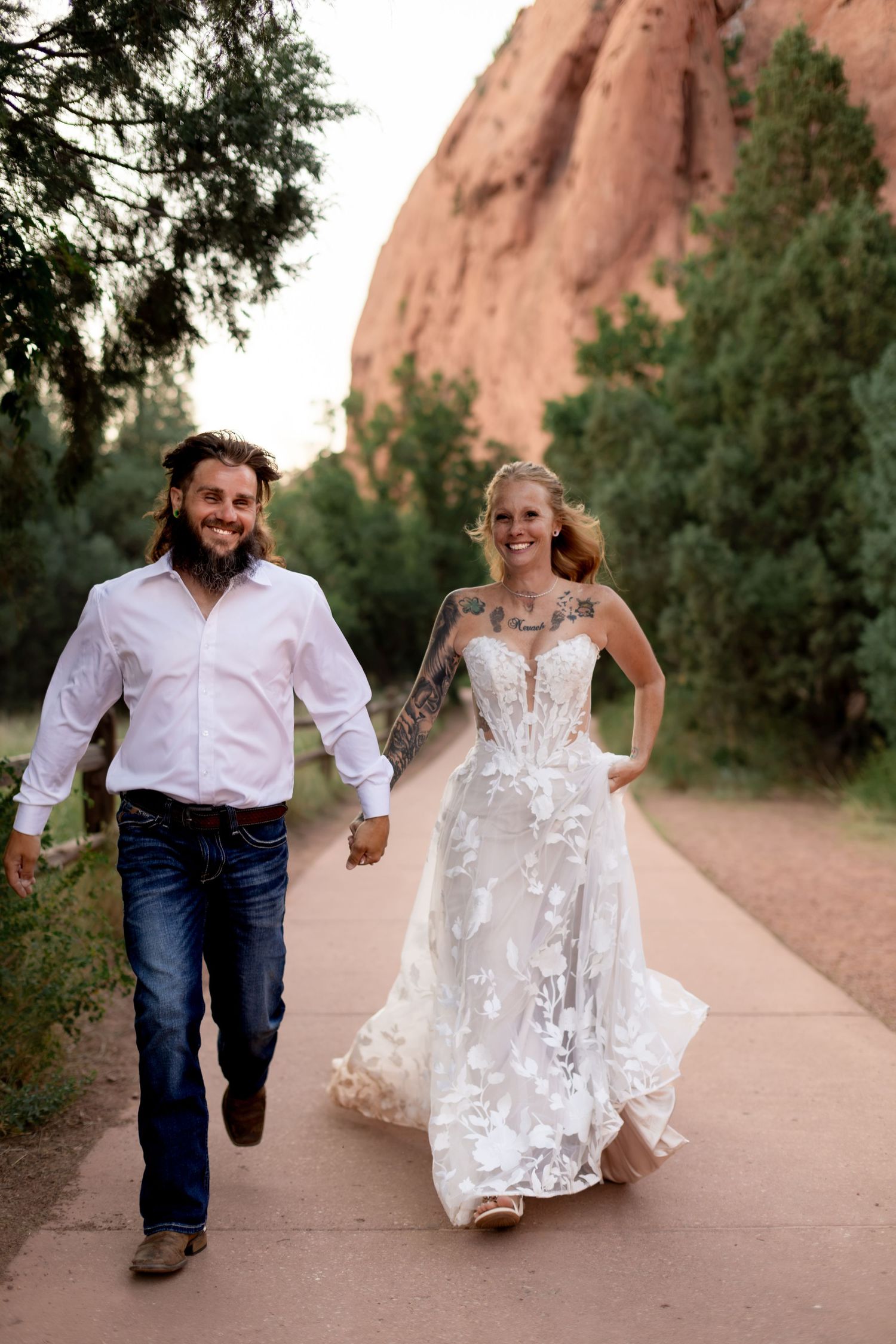 Joyful bride and groom holding hands running on a path with red rock formations at Garden of the Gods.