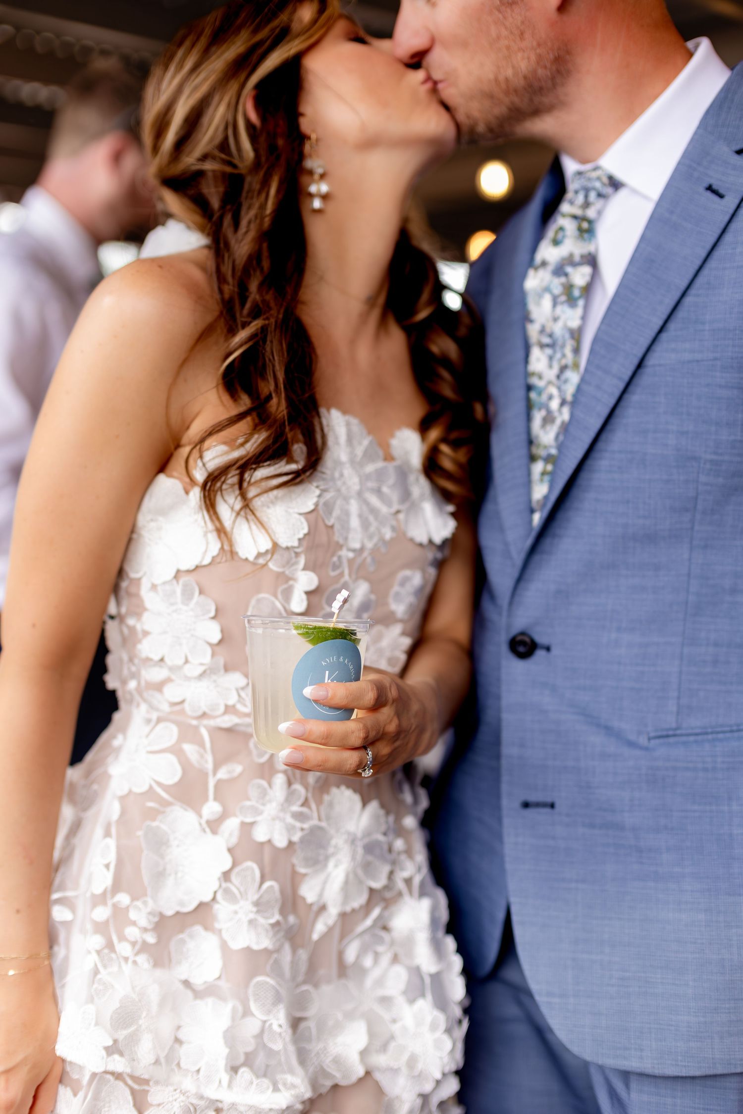 Bride and groom share a kiss while bride holds a cocktail at their wedding reception.